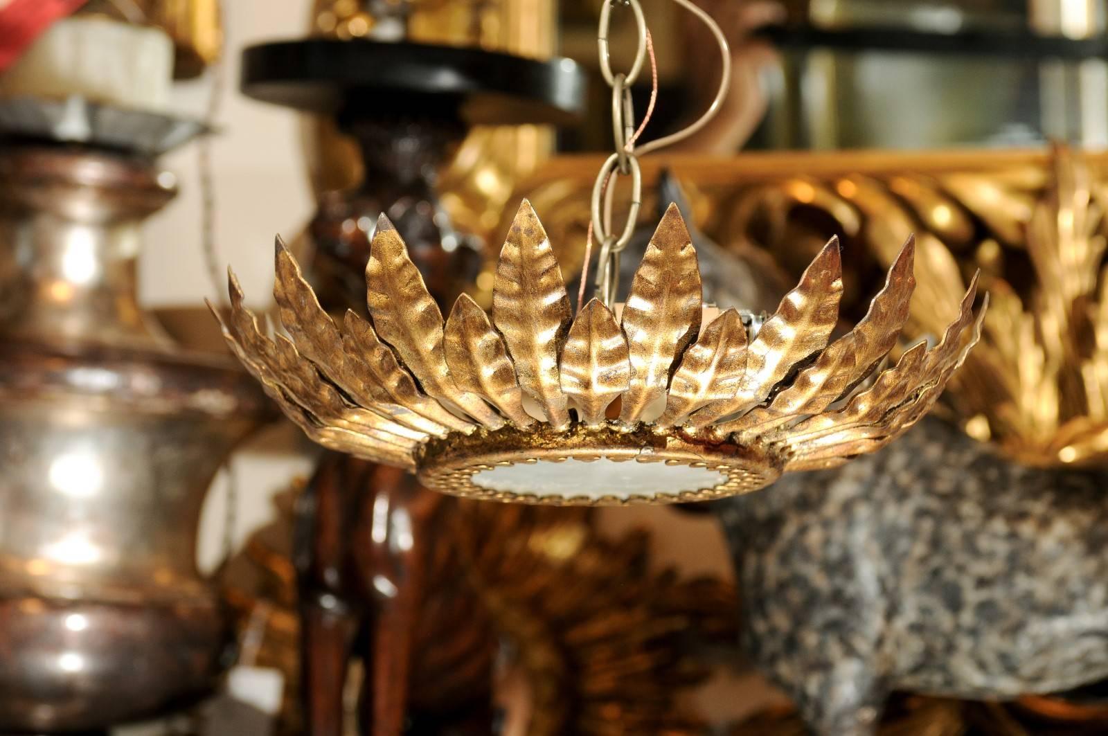 This petite Spanish mid-20th century crown semi-flush chandelier is made of gilt metal and frosted glass at the bottom. The surround is adorned with leaf motifs of two different sizes, curving towards the centre of the light fixture. The two lights