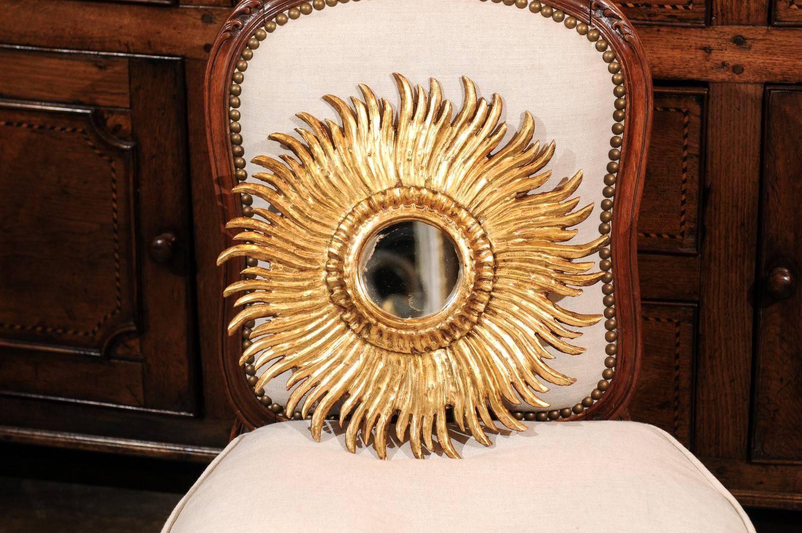 This French vintage sunburst mirror features a small size round mirror framed by a carved giltwood molding. On the surround, an exquisite décor of wavy sunrays of variating sizes, gives life to the mirror. In great condition, this French sunburst
