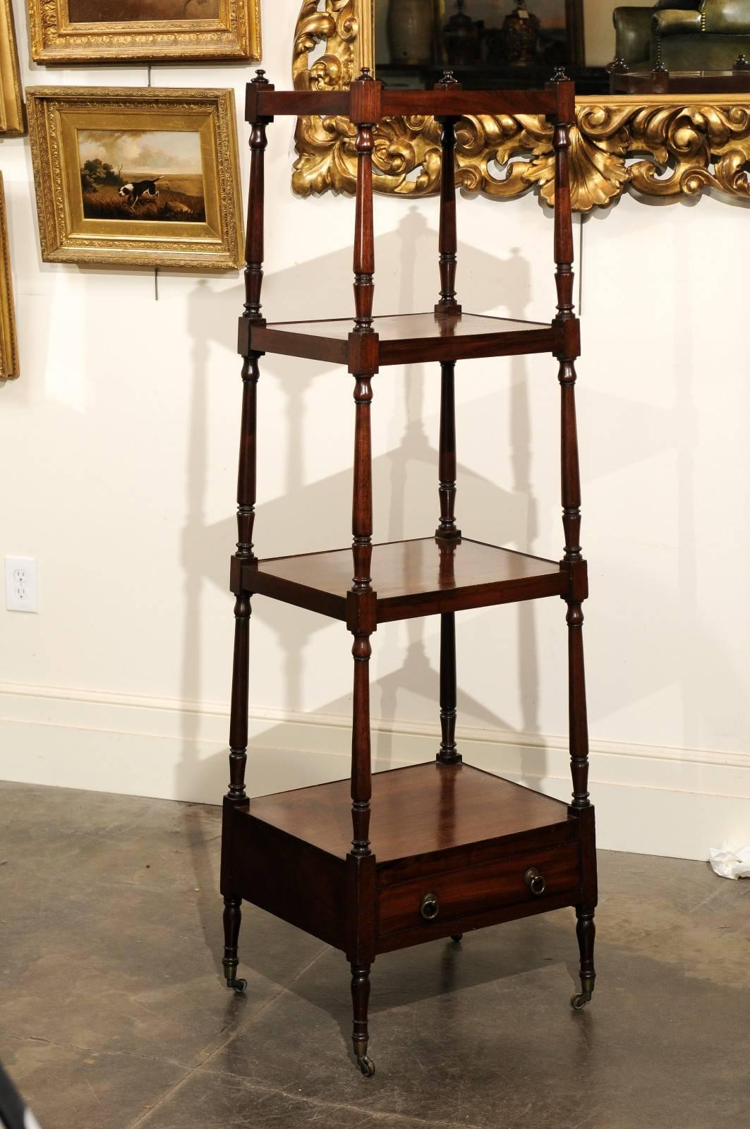 This English mid-19th century mahogany trolley features four graduated shelves over a single drawer. The shelves are secured by four turned supports on the sides, topped with discreet finials. The single drawer placed in the lower section opens with