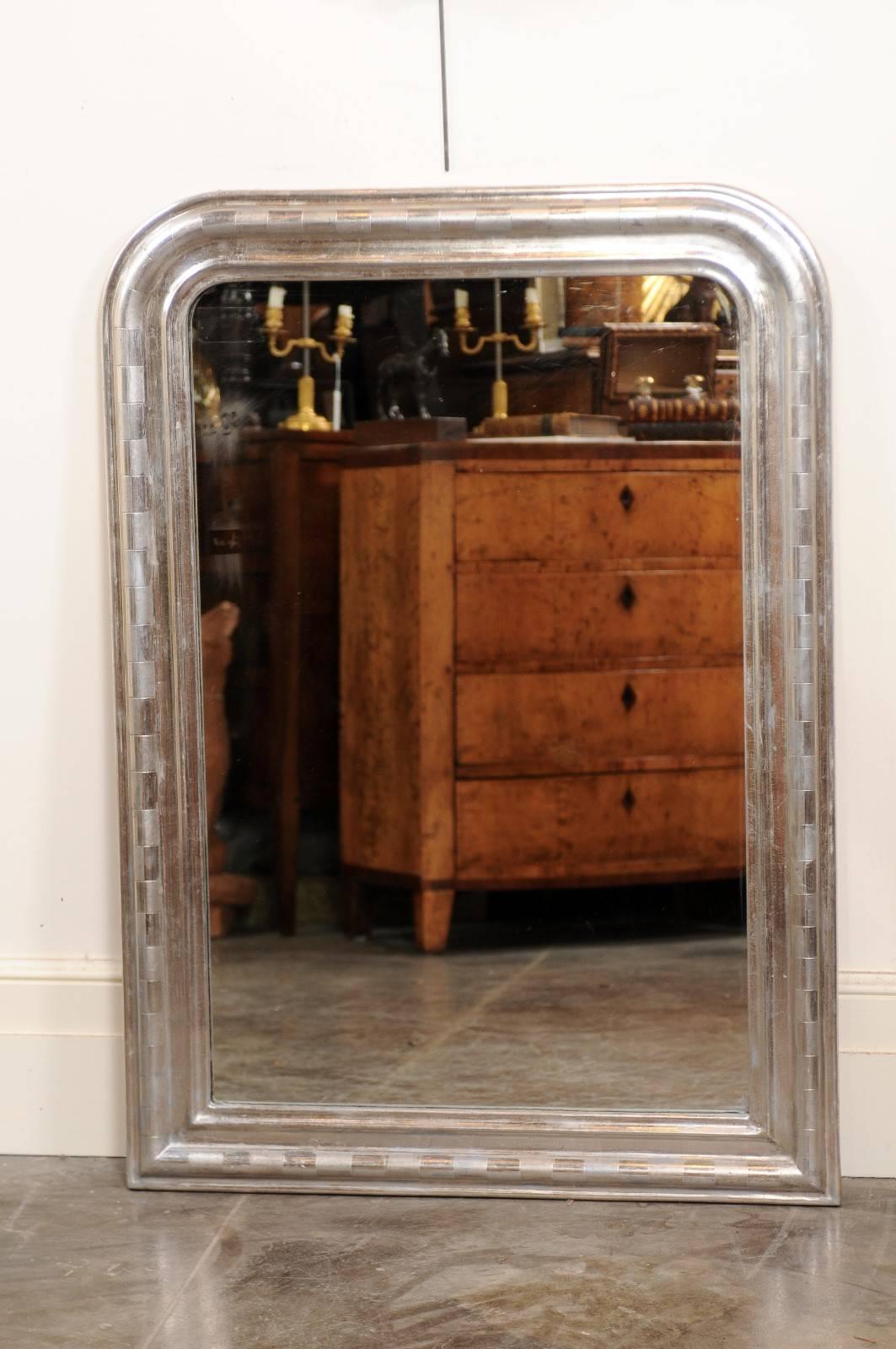 This French Louis-Philippe style mirror from the turn of the century (19th-20th) features rectangular, vertical silver leaf gilded frame with rounded edges. The frame is adorned with a combination of shiny and mat silver motifs, reminiscent of a