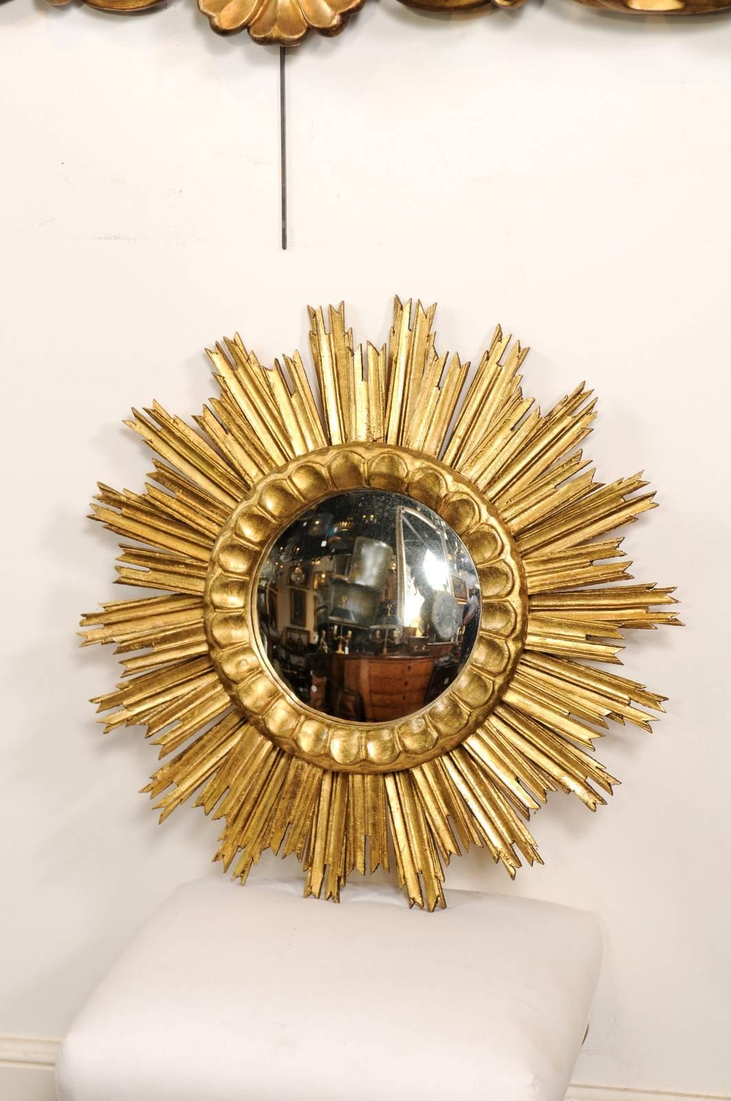 A French sunburst mirror with convex glass in a giltwood frame. This Mid-Century mirror is set in a circular frame with a ring of exquisite petal motifs. Surrounding the ring is a bevy of veined sun rays of alternating heights. This lovely sunburst