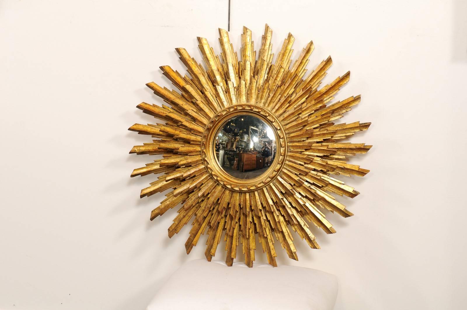 This French sunburst mirror from the mid-20th century features a small circular mirror in the centre, surrounded by three layers of giltwood radiating sunrays. The carved molding framing the mirror gives birth to the smallest sized sunrays, placed