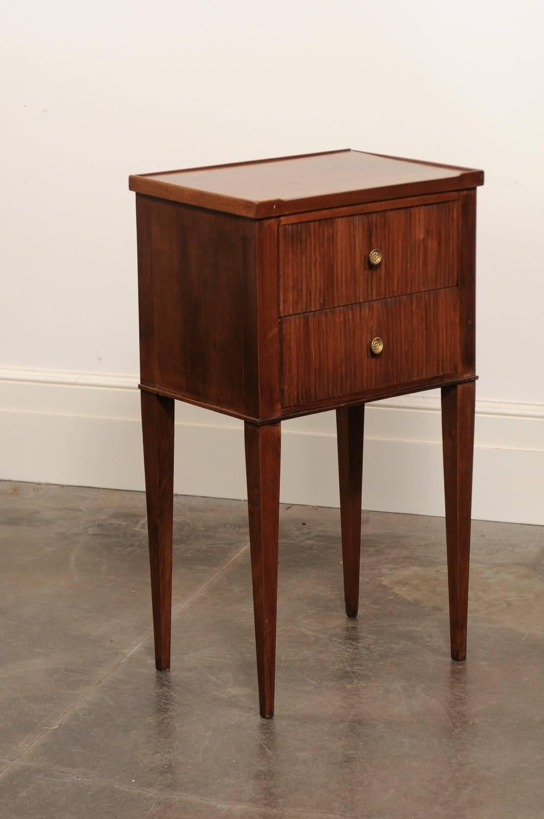 This French mahogany side table from the turn of the century features a rectangular three-quarter gallery tray top over two drawers with reeded décor and brass pulls. The piece is raised on four slender tapered legs. The simplicity of the clean