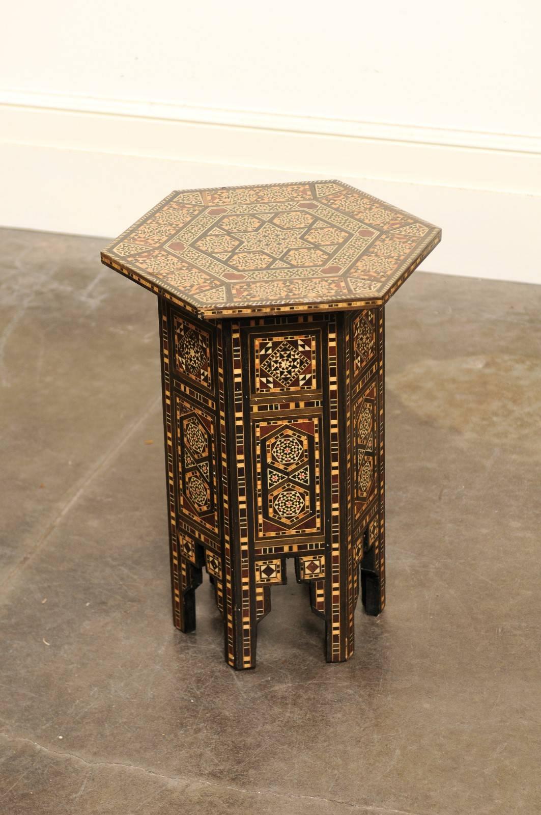 This petite Moroccan drinks table from the Mid-Century features an hexagonal top adorned with a delicate wood and bone inlay depicting an elaborate geometrical design with central star. Each panel of the hexagonal base shows a sumptuous decorative