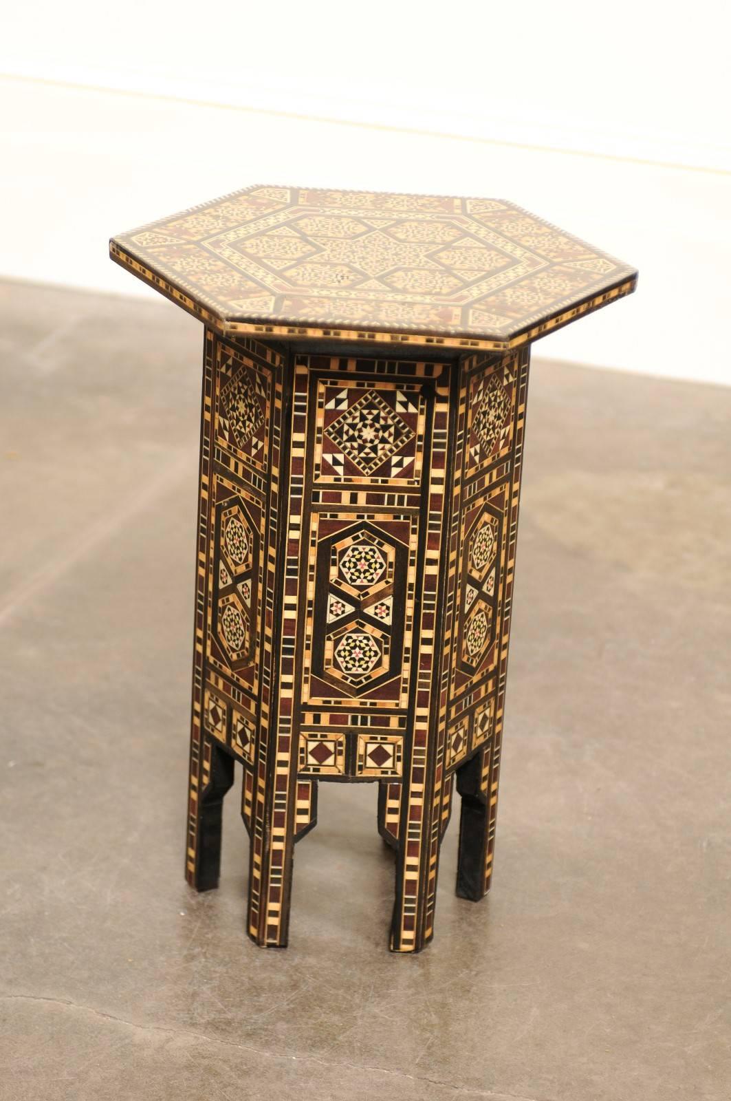 This petite Moroccan drinks table from the Mid-Century features an hexagonal top adorned with a delicate wood and bone inlay depicting an elaborate geometrical design with central star. Each panel of the hexagonal base shows a sumptuous decorative