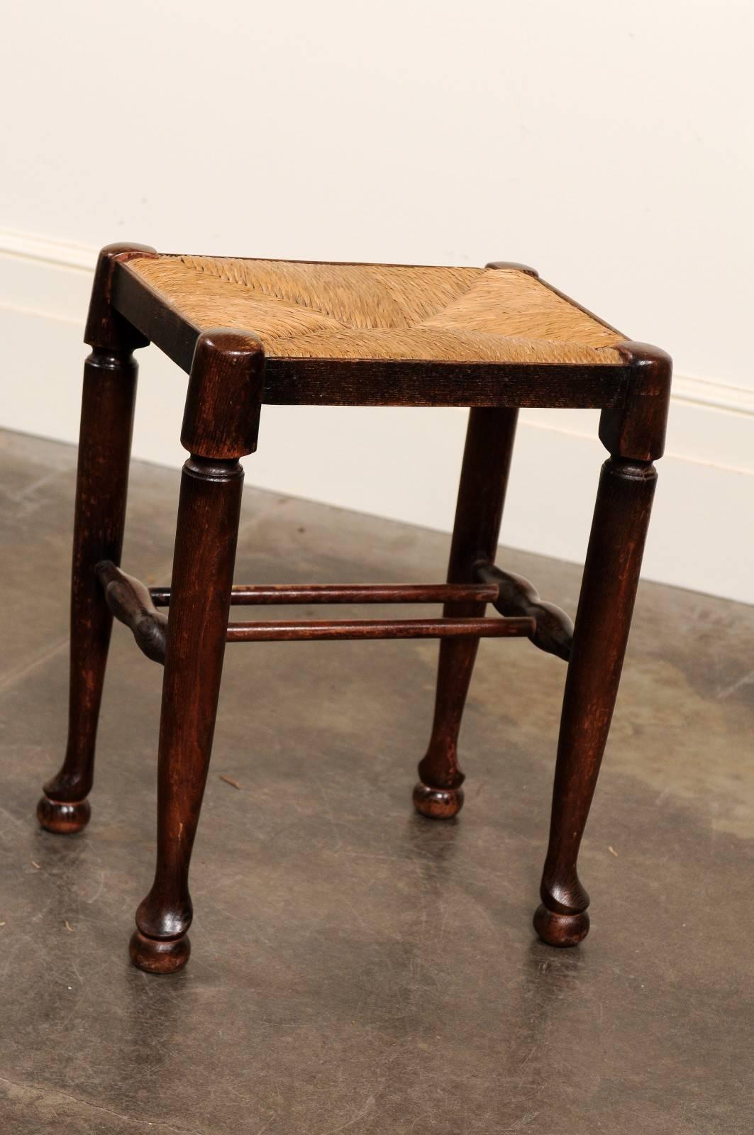 This English oak stool from the late 19th century features a rectangular rush seat over four sleek legs with spade ends raised on ball feet, secured with an original double cross stretcher. The beautiful rich patina, combined to the simplicity of