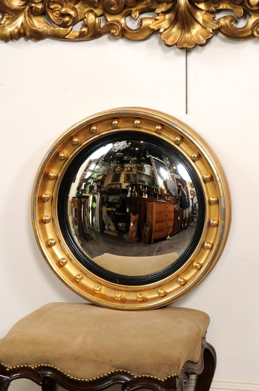 This English girandole mirror from the mid-19th century features a circular convex mirror surrounded by an ebonized wood molding. The outer frame is made of giltwood and adorned with small spheres, rhythmically placed on the surround. Elegant in
