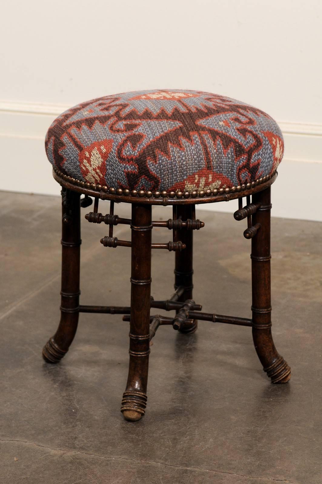 This French turn of the century Chinese Chippendale style dark walnut stool features a circular upholstered seat over an intricate base. The four splayed legs are delicately decorated with geometric motifs and joined together by an exquisite cross
