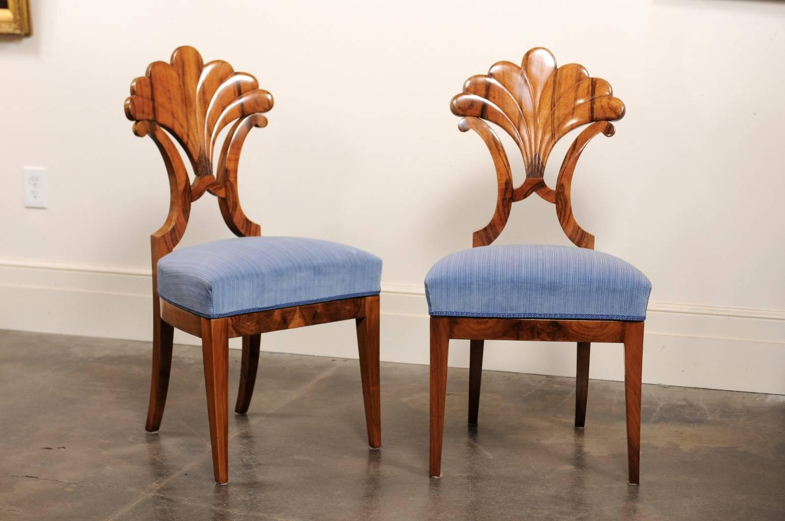 This pair of exquisite Biedermeier side chairs from the mid-19th century features fan shaped backs over light blue upholstered seats. The chairs, made of walnut, are raised on two front tapered legs and two saber legs in the back. The sleek, simple