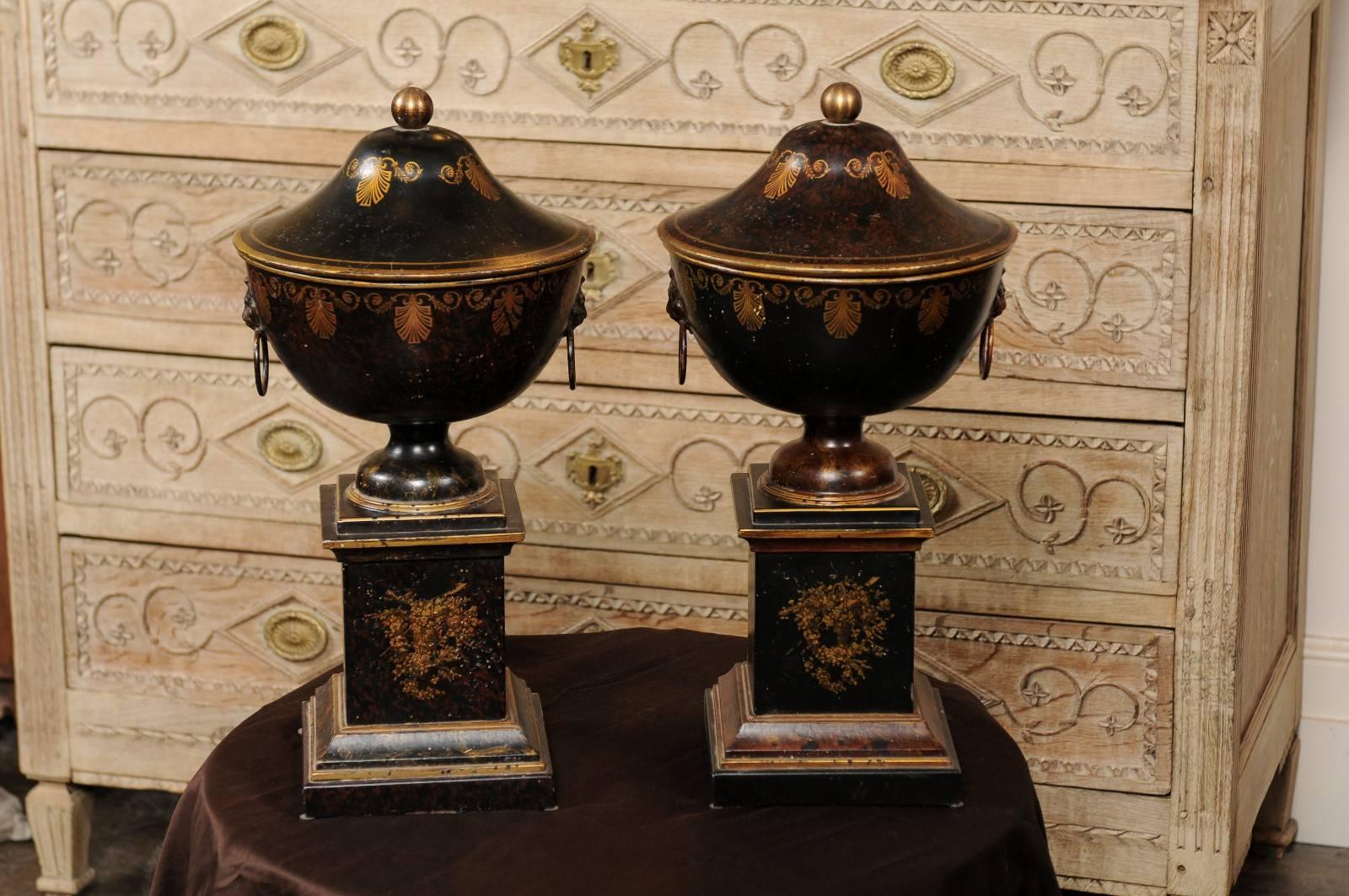 20th Century Pair of French 1920s Tole Black Tole Urns on Pedestals with Gilded Accents