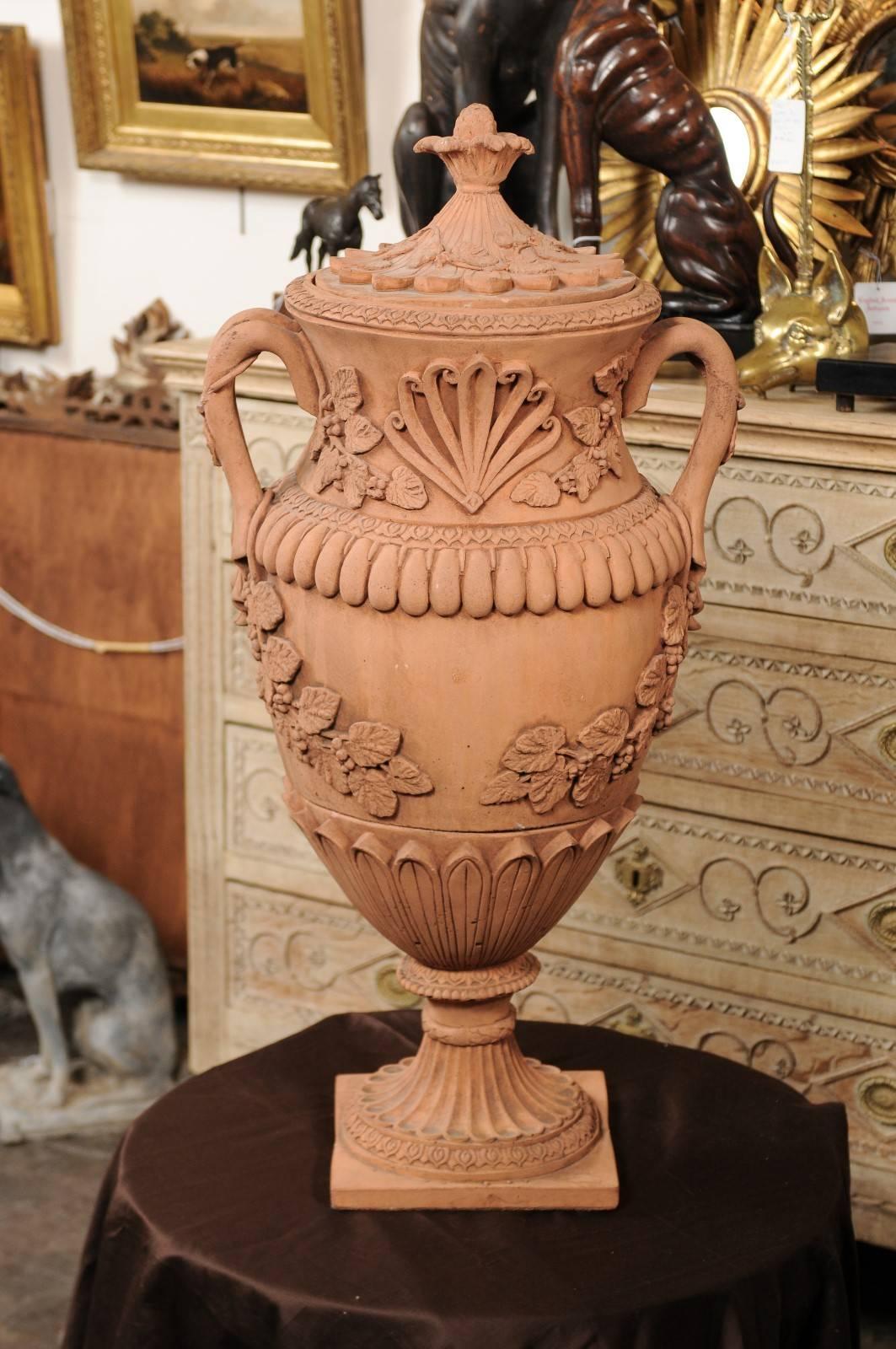 An exquisite pair of large size French terracotta urns from the early to mid-20th century. These urns are made of three parts. Each is adorned with a beautifully decorated lid with pinecone motif, flower and grapes over petals. The motif of the vine