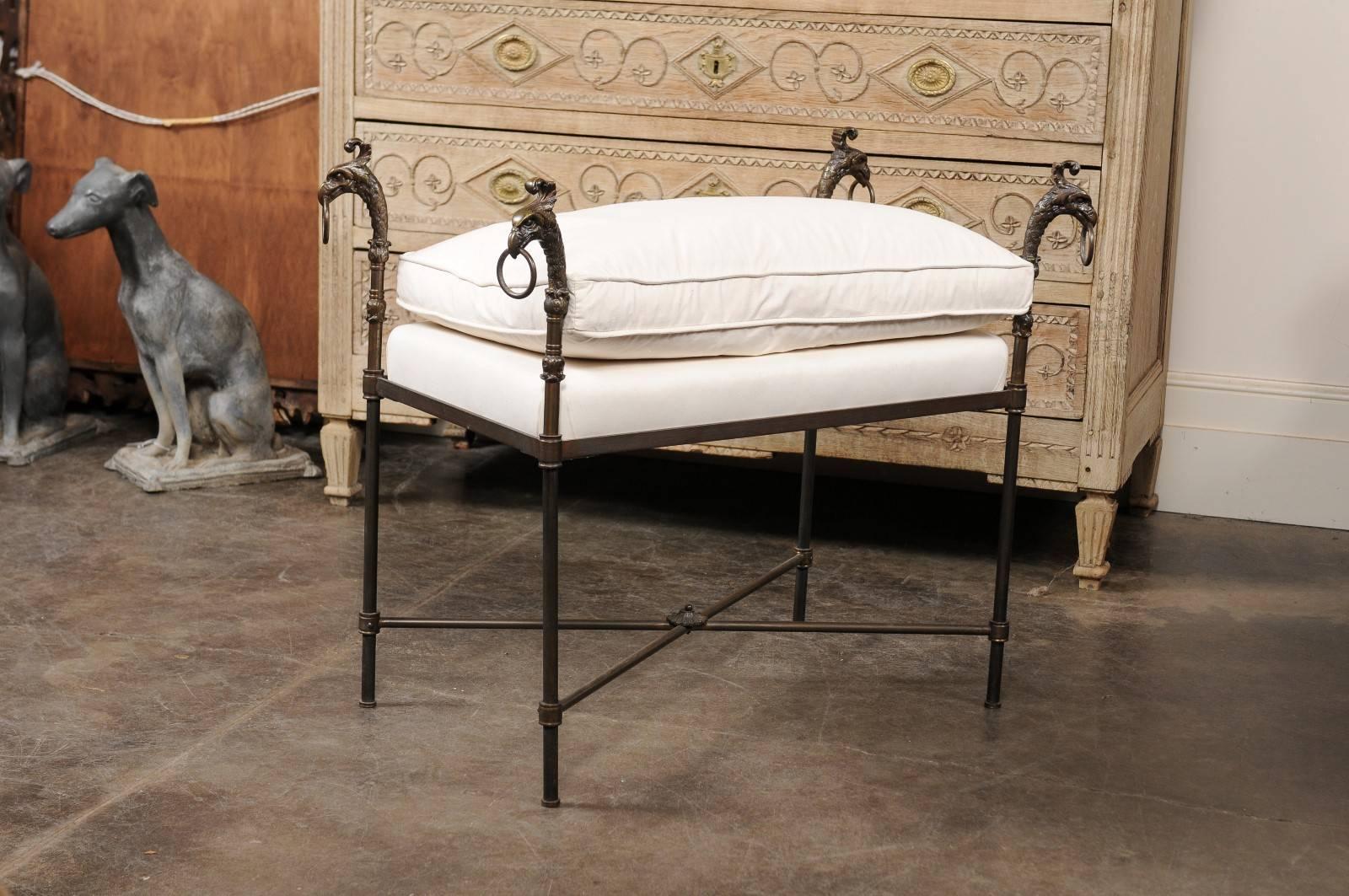This French iron stool from the turn of the century (19th to 20th century) features a rectangular smooth muslin upholstered seat with comfy cushion, supported by four iron legs adorned in their upper section with exquisite bronze griffin heads with