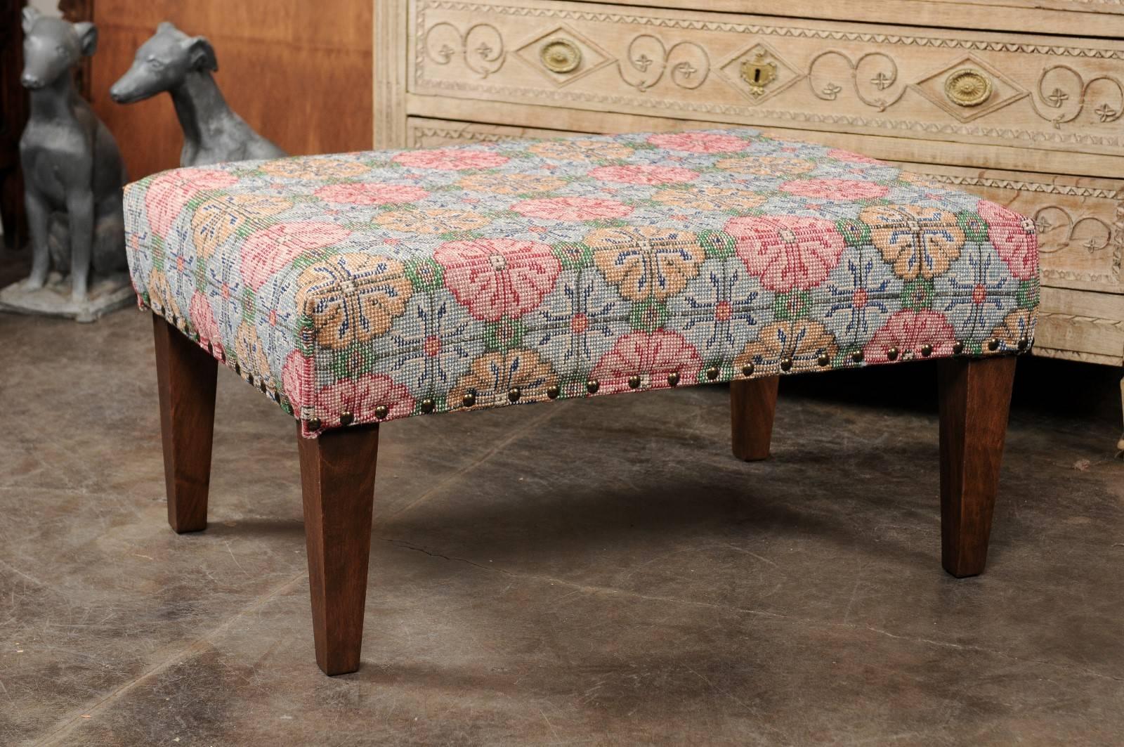 A Turkish upholstered ottoman with floral motifs from the midcentury on custom wood tapered legs. This ottoman features a rectangular seat, upholstered with a vintage Turkish wool rug, adorned with colorful floral motifs ranging from pink to light