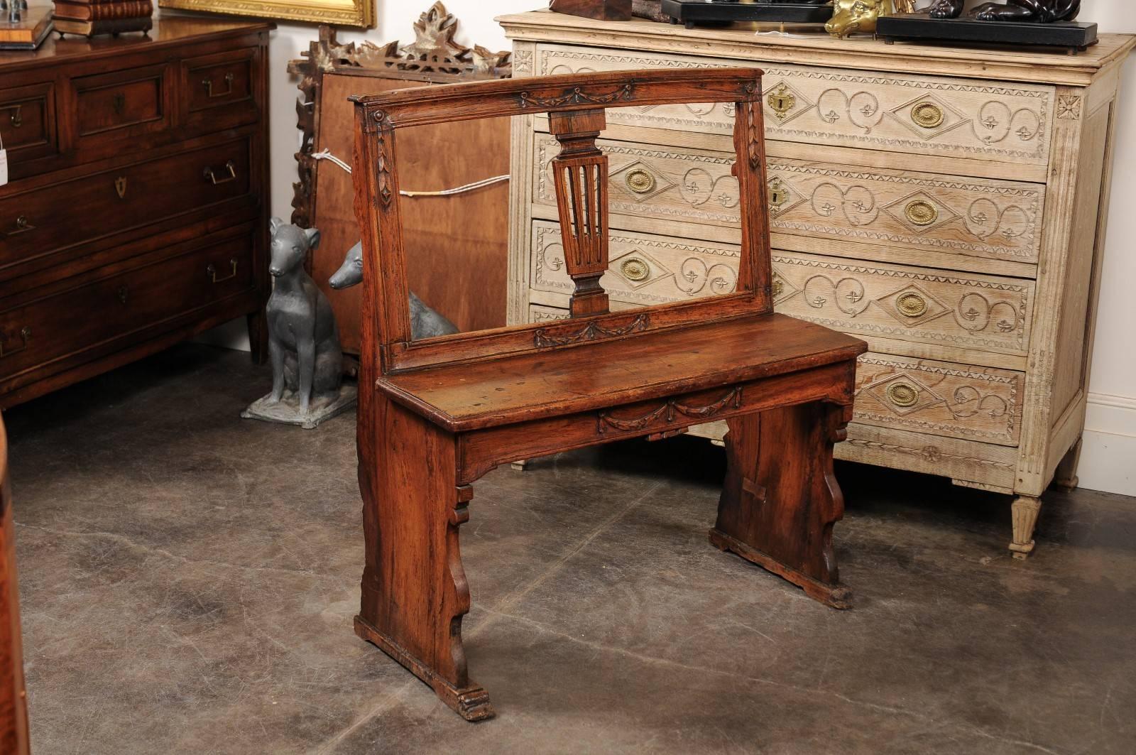 This exquisite Italian walnut bench from the late 18th, early 19th century features a slightly slanted carved back with central pierced and reeded splat adorned with swag motifs in the crest. The piece also features an elegantly carved seat rail.