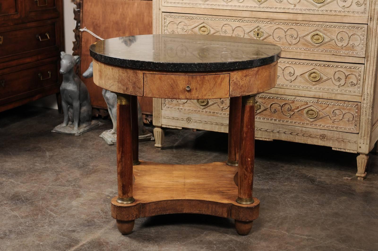 This French Empire style side table from the mid-19th century features a circular black marble top sitting over a beautifully burl veneered apron with two hand-cut, dovetailed drawers and two pull-outs fitted with leather. The table is supported by