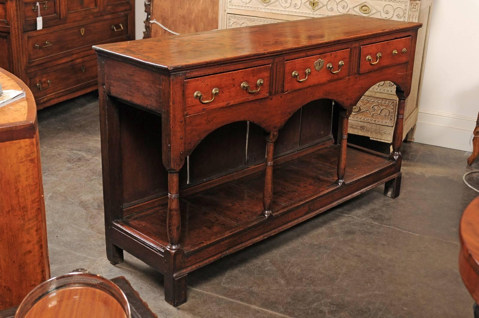 This English George III oak and fruitwood server dresser base from the late 18th century features a rectangular top over three drawers and a lower shelf. Each drawer is adorned with brass hardware, the central one with the addition of an escutcheon.