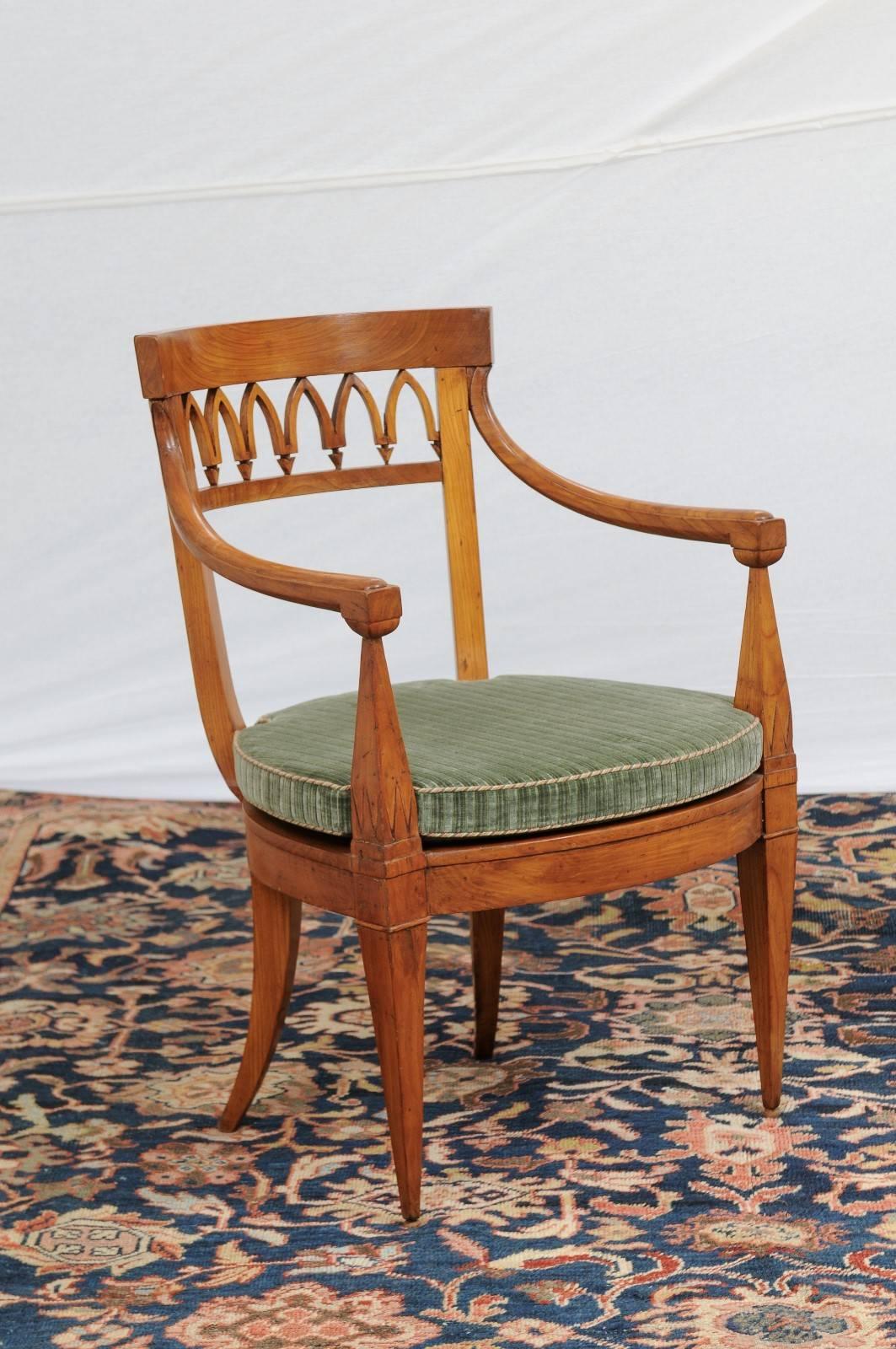 A pair of Austrian Biedermeier armchairs from the mid-19th century with pierced back, cane seats and seat cushion. Each chair features a pierced design on the back, reminiscent of Gothic ribbed vaults over curved arms with obelisk shaped supports.