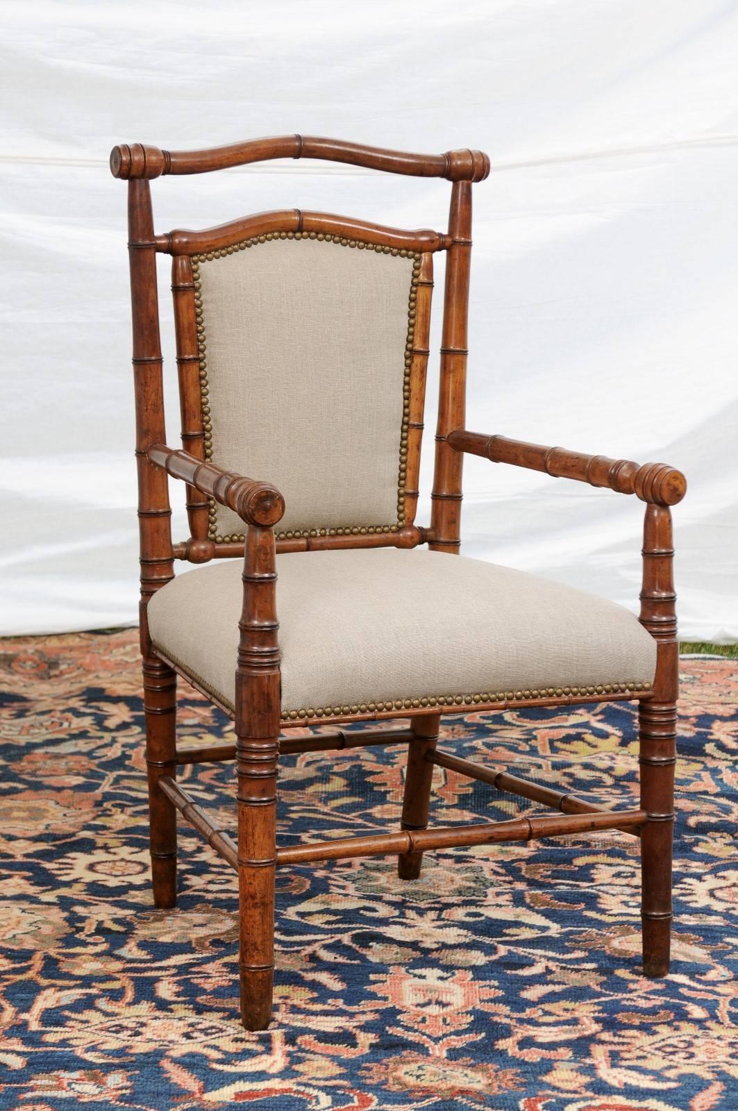 This English faux-bamboo armchair from the turn of the century features a slightly slanted back with partial upholstery and nailhead trim over turned legs with side stretchers. The straight lines seen on the arms, legs and stretchers are gently