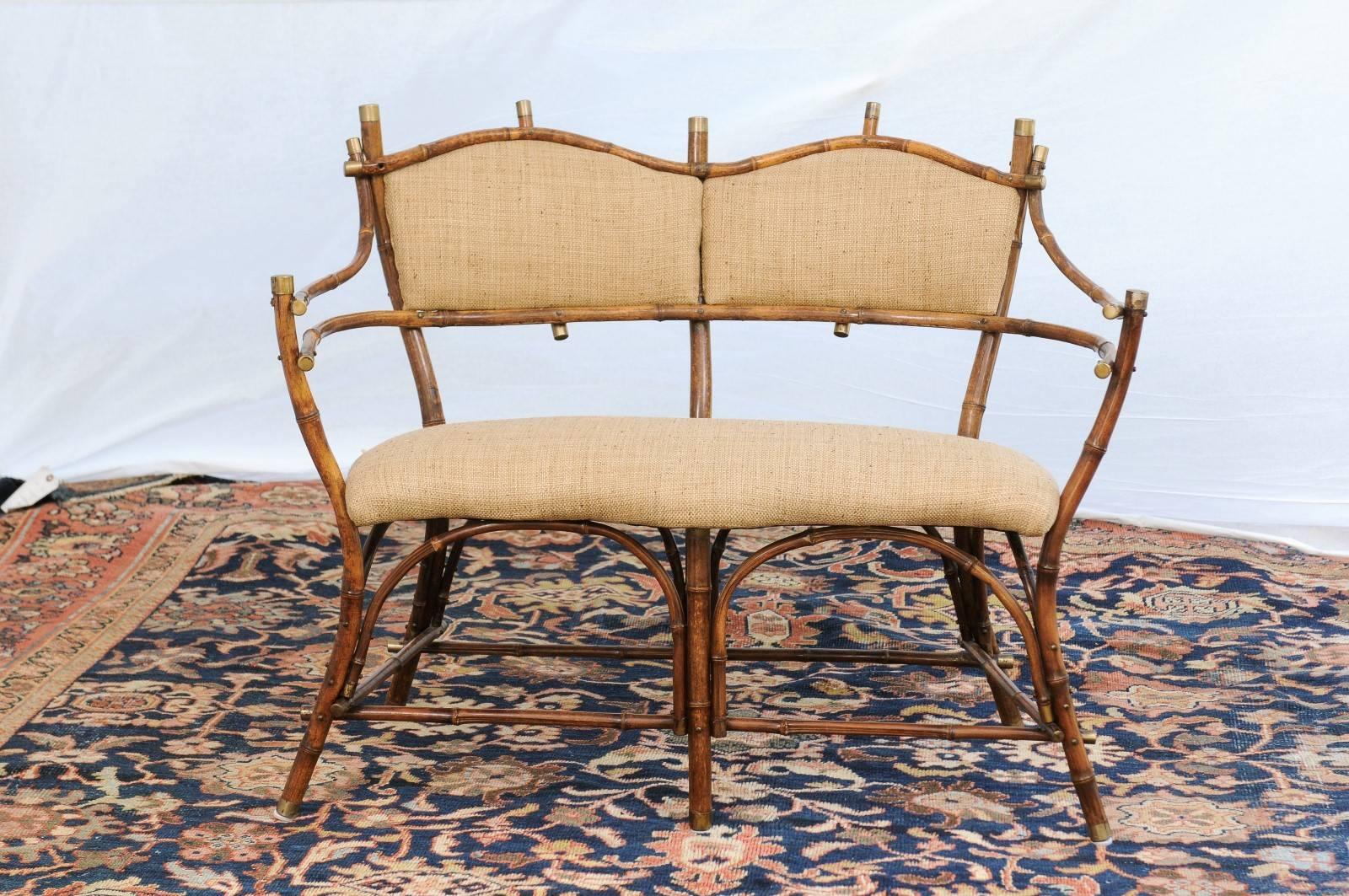 This English Edwardian period bamboo settee from the turn of the century features a two-seat open back with nicely curving armrests. The upholstered seat is raised on six legs with side stretchers. The Silhouette is accentuated with brass accents at