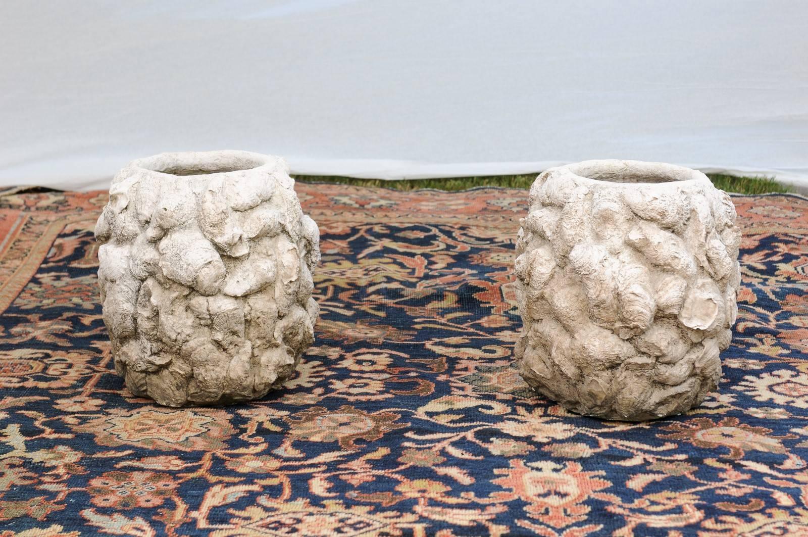 This pair of vintage concrete shell planters from the 1950s features round bodies adorned on their surround with a myriad of oyster shells. Created in a medium size, they are quite heavy. Their interesting decor and white color would make this pair