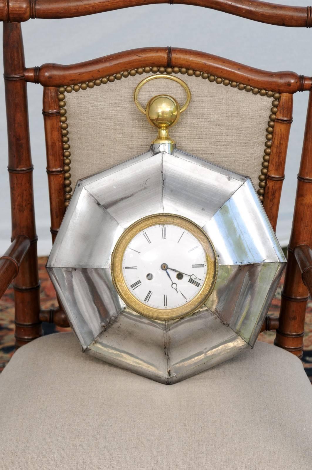 This French small size wall clock from the late 19th century features an octagonal steel frame highlighted with brass accents. The clock is whimsically shaped like a pocket watch, with the typical circular bow at the top, which surrounds a watch's