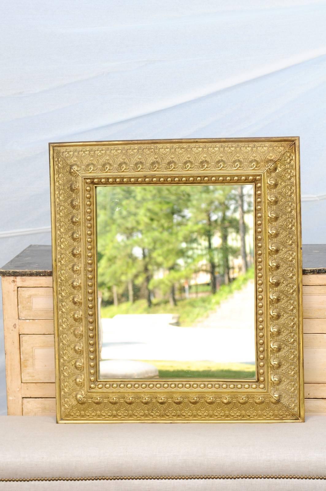 This Dutch gilded mirror from the late 19th century features an exquisite bevelled repoussé brass frame. The wonderful frame is made of a rhythmic repetition of floral motifs delicately protected by intertwined volutes shaping a succession of