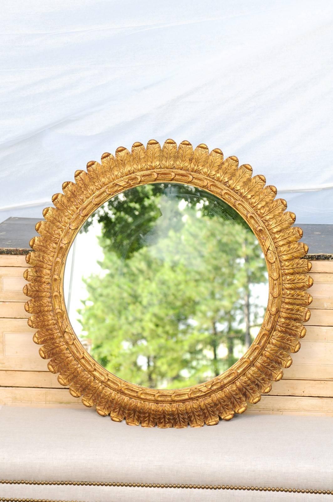This French giltwood circular mirror from the mid-20th century features a clear central mirror providing great reflection, surrounded by a carved foliage themed frame. The inner molding, closer to the glass, is adorned with oblong carved motifs