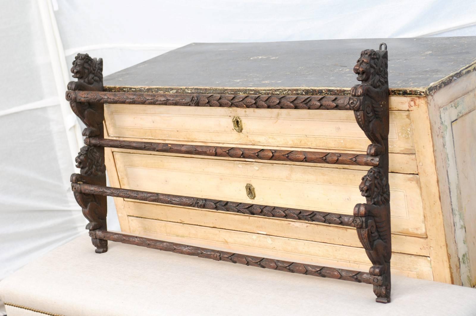 An English oak rack with carved lions from the late 19th century. This English wooden rack is made of four rows of carved beams, secured on both sides with carved lions with volutes in the front. Carefully guarding your possessions, the lions have