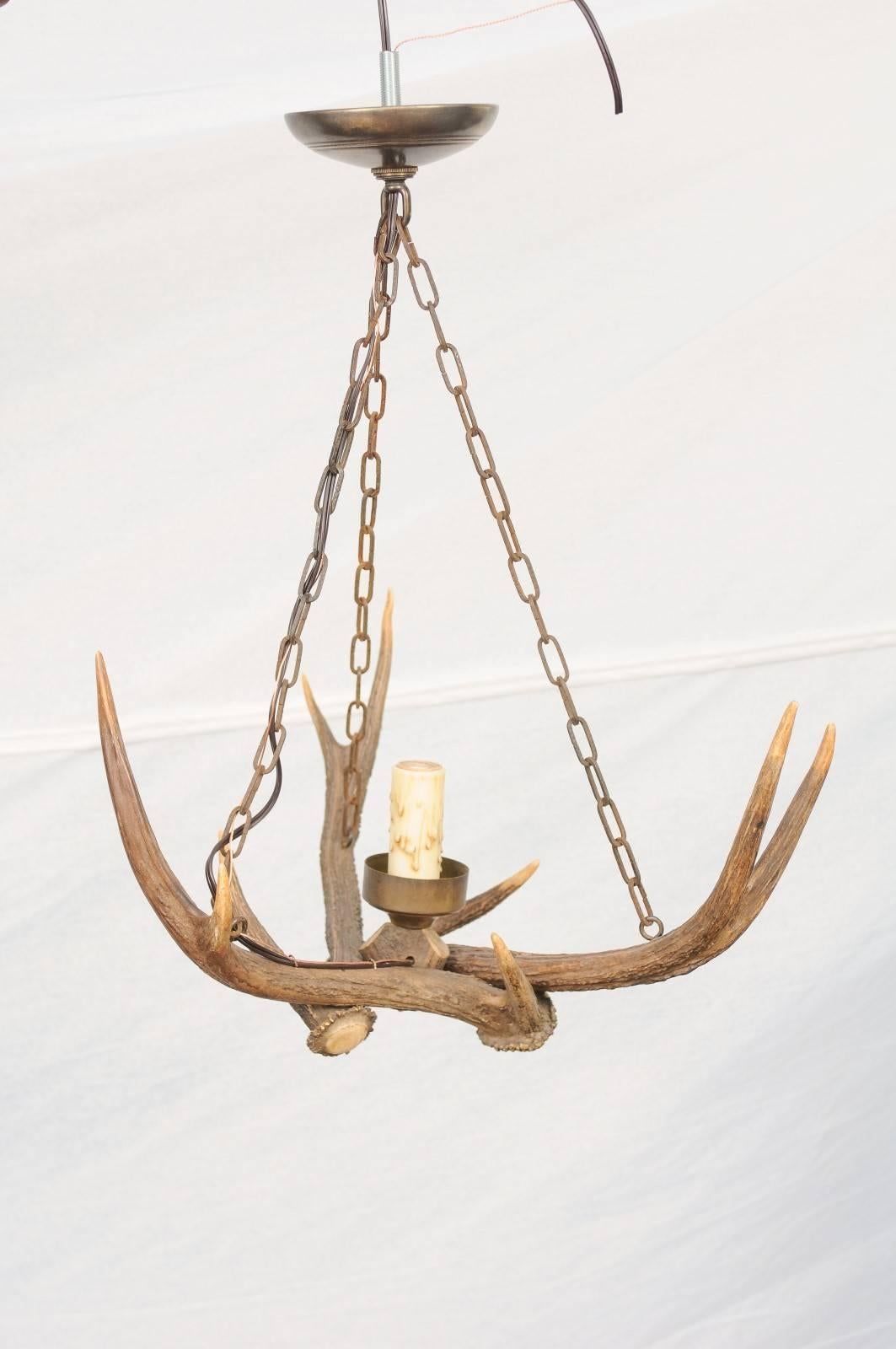 This French antlers chandelier from the early 20th century features a central single light concealed inside an authentic wax candle sleeve. We currently have two available, priced and sold individually. Raised on a simple round metal bobèche, the