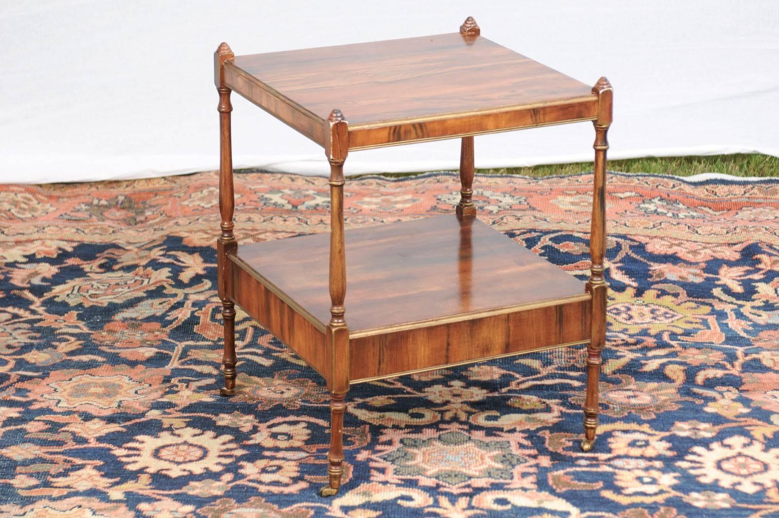 This English two-tiered side table on casters from the early 20th century features a faux-bois painted square top with traces of gold accents on the trim, over a lower shelf with single drawer. The sides are flanked with four thin columns with