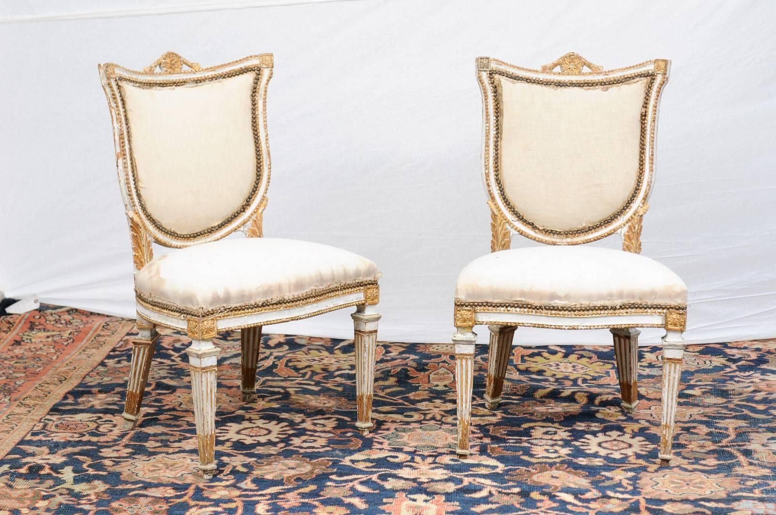 This pair of Italian neoclassical painted and giltwood side chairs from the late 18th century is quite a show stopper! Each chair has a shield-shaped back, adorned on the crest with a medallion receiving in its center a delicate carved flower topped