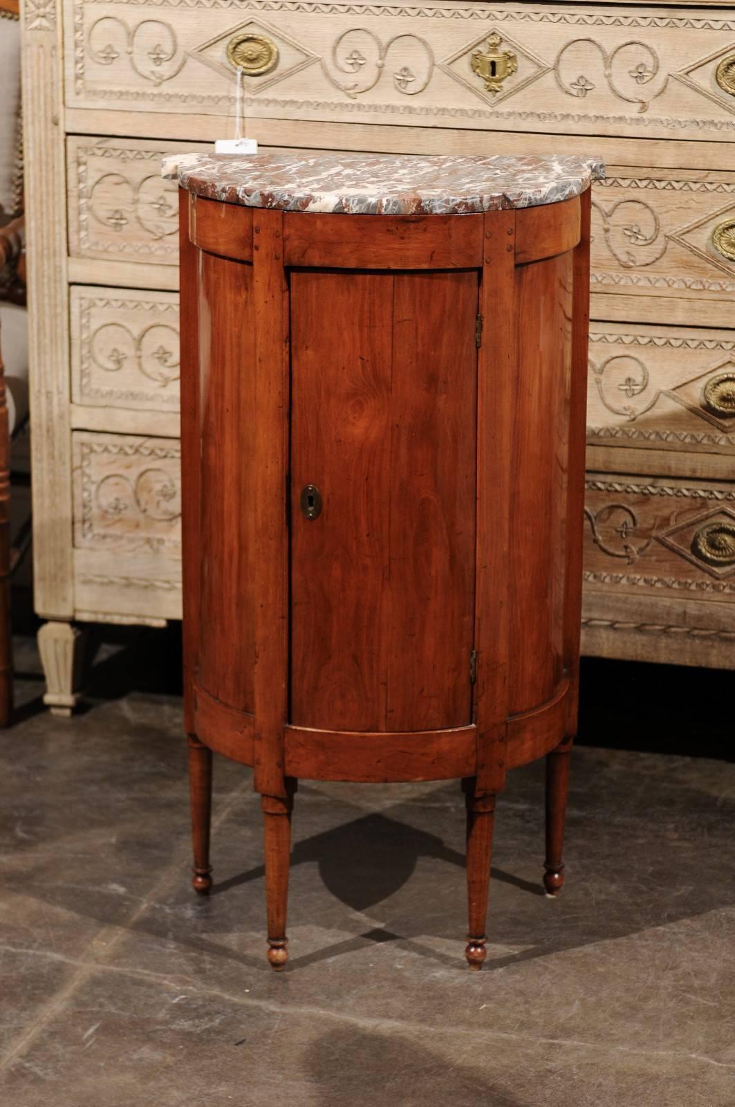 French Directoire style fruitwood demilune cabinet with marble top from the early 19th century. This exquisite French single door fruitwood cabinet features a brown and grey shaped marble-top over a pegged convex base. A single door opens to reveal