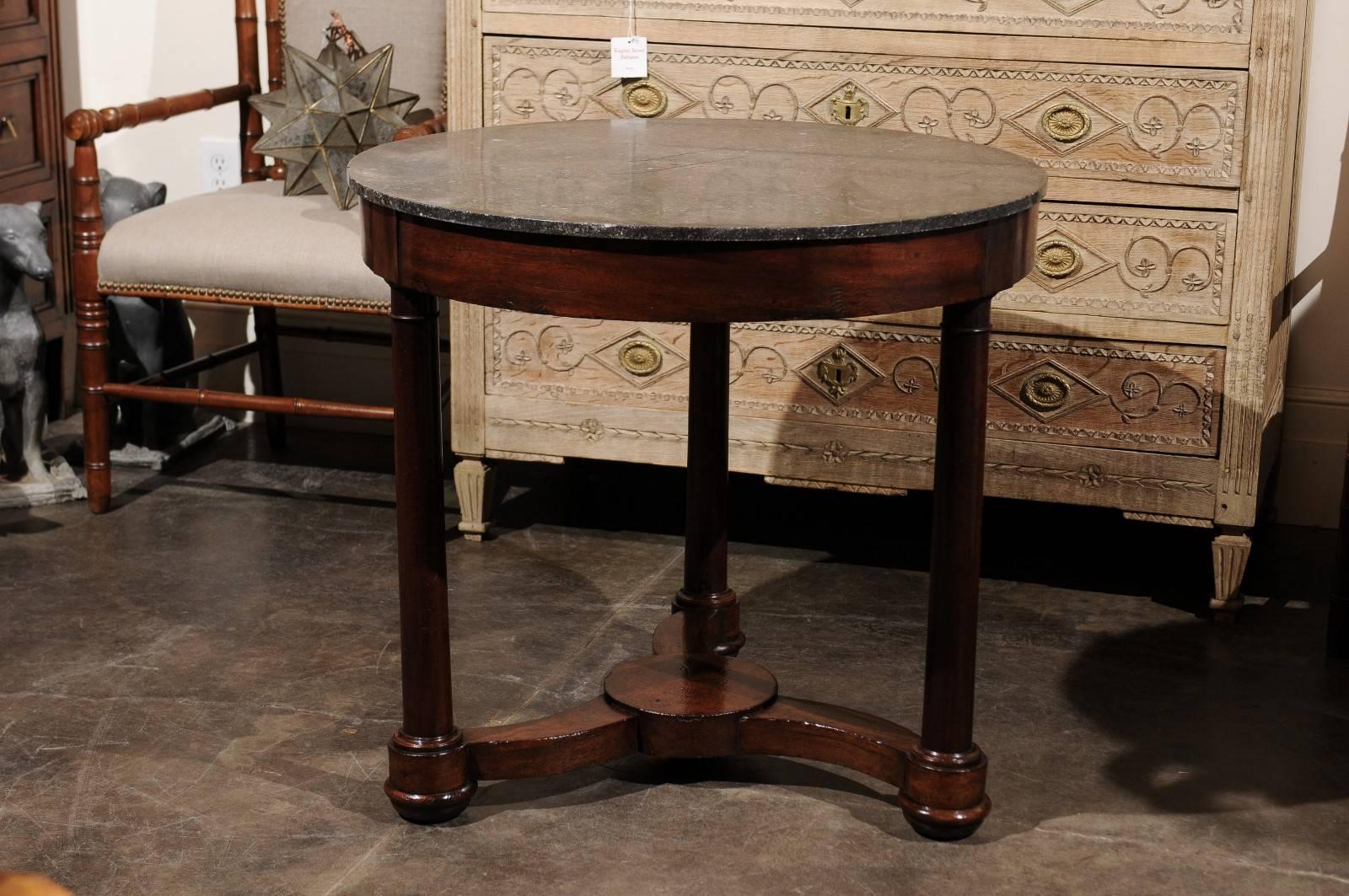 A French mid-19th century Empire style mahogany table with dark grey marble top over a tripod base with cross stretcher. This French center table was born circa 1840, not long after the fall of the French First Empire. Typical of the Napoleonic