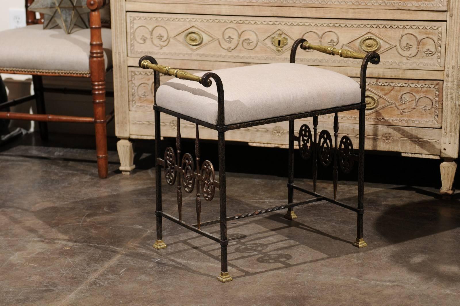 Italian wrought iron bench with bronze accents and upholstered seat from the early 20th century. This Italian 1920s bench features a wrought iron frame supporting a rectangular linen upholstered seat. The delicately out-scrolled arms are highlighted