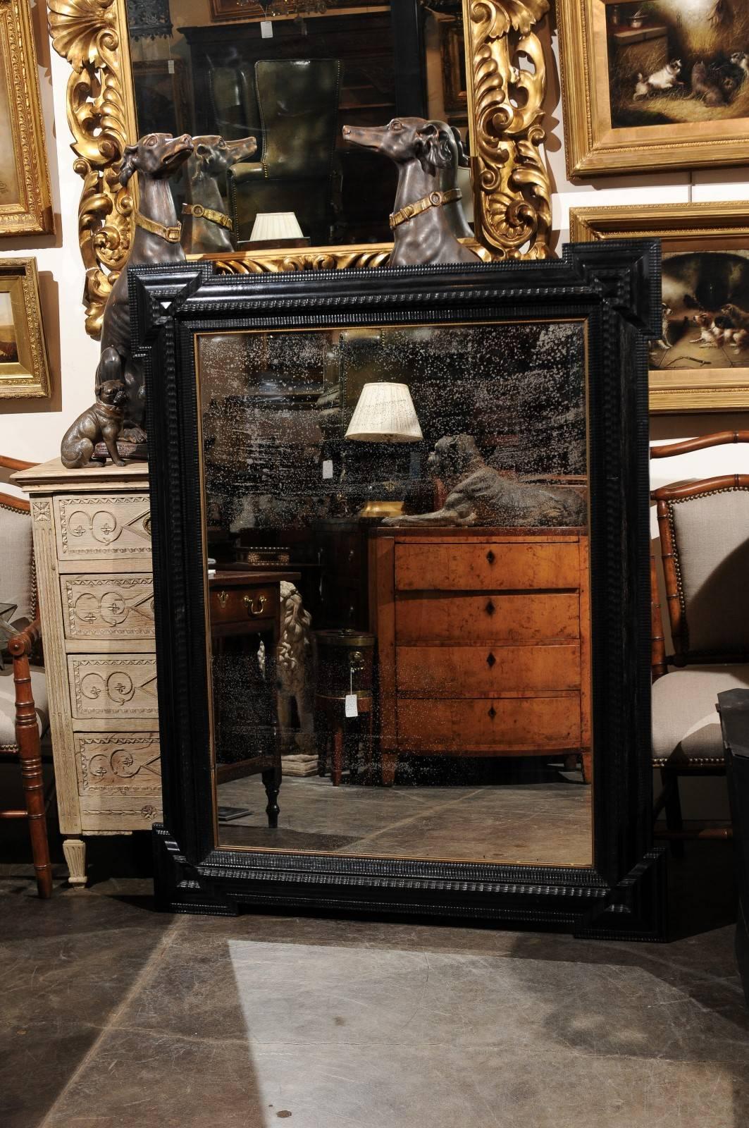 Large size ebonized and carved wooden Dutch mirror with distressed glass from the early 20th century. This oversized Dutch mirror features a linear black frame, typical of the northern Europe style and one could easily imagine such a mirror depicted