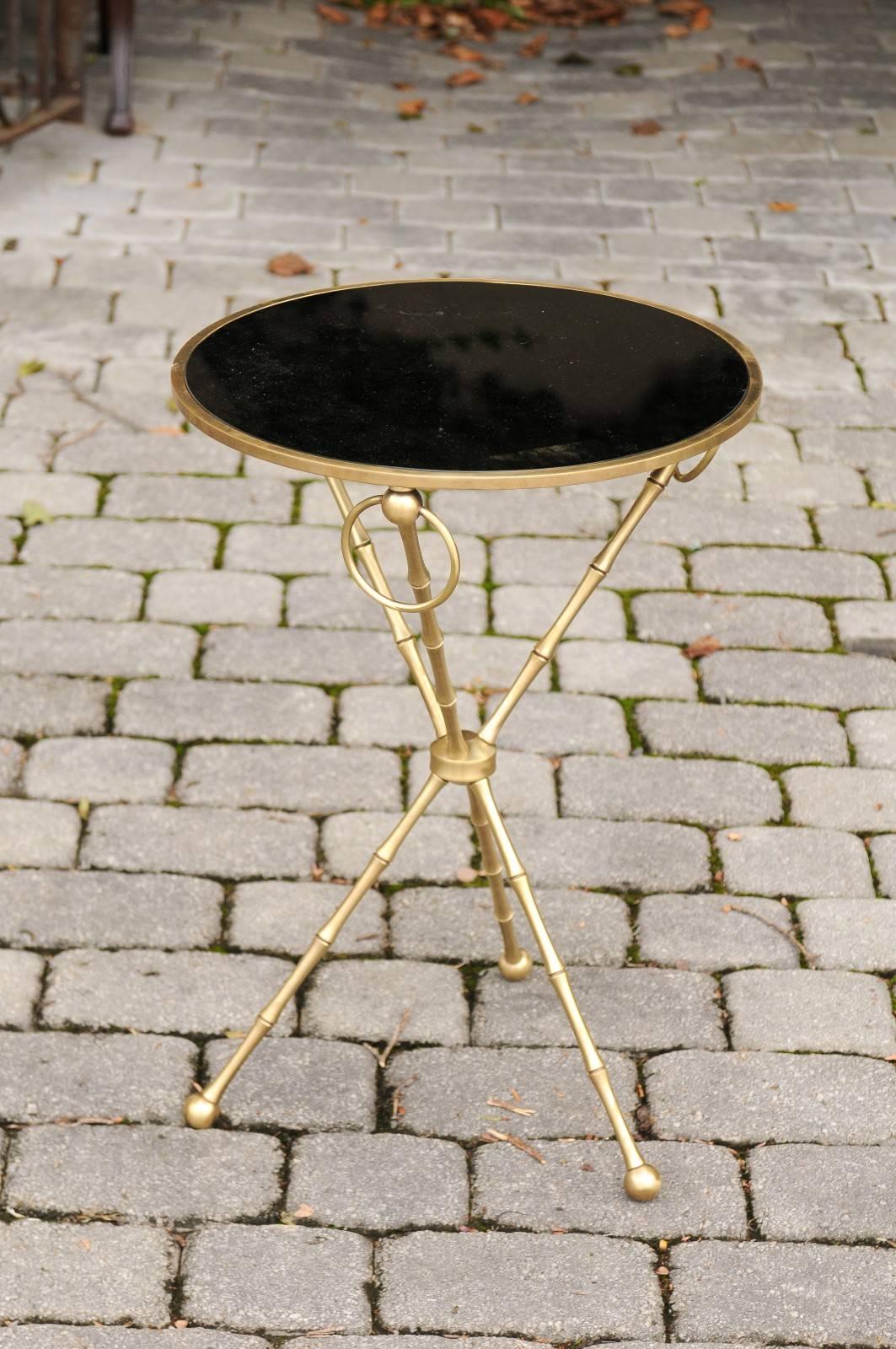 A French Maison Jansen style round side table with brass and black glass from the midcentury. This French side table was born in the 1940s and produced in the manner of Maison Jansen. The circular top is adorned with black glass, safely secured in a