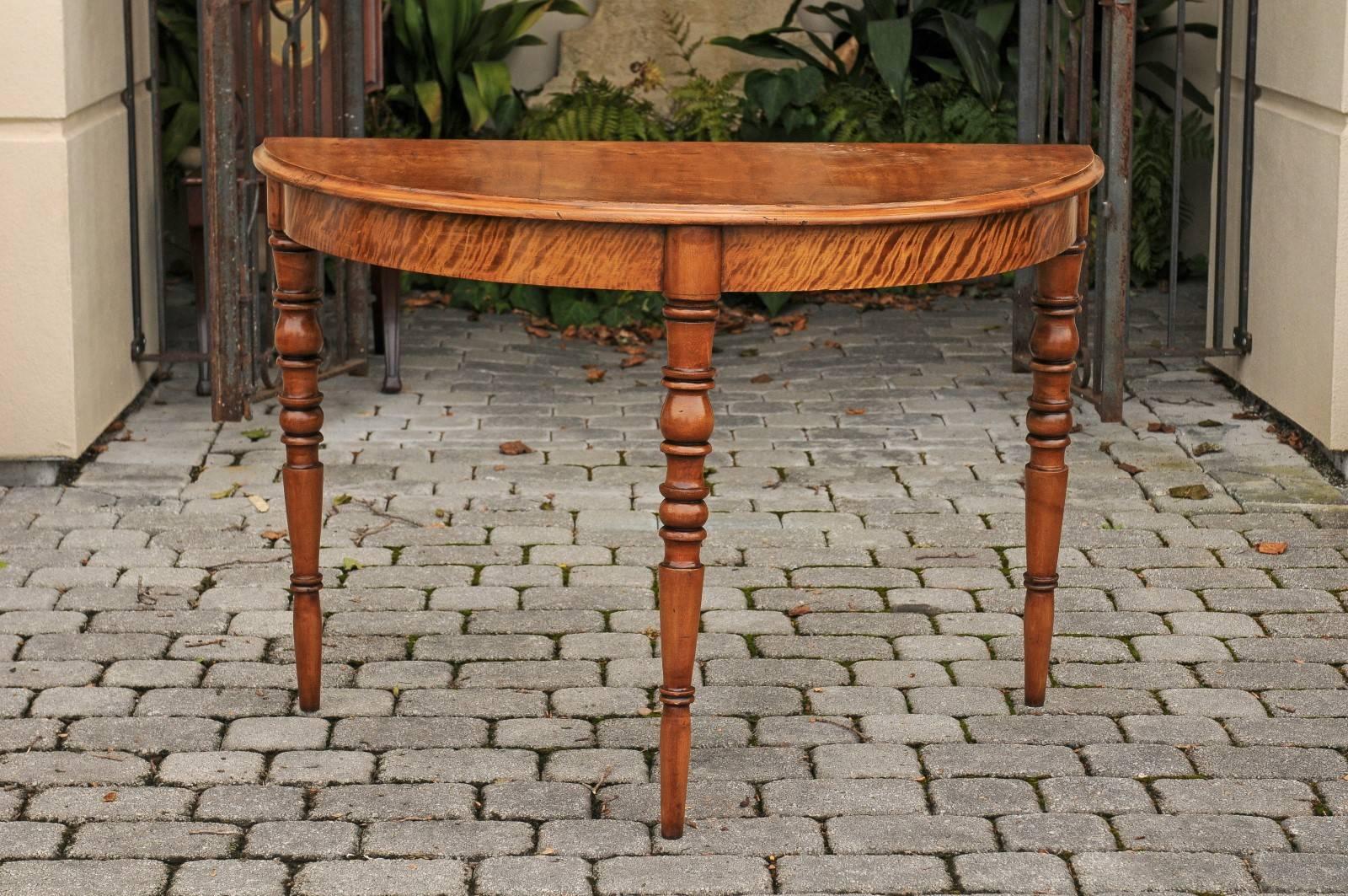 A pair of French Louis-Philippe period maple demilune consoles tables with turned legs from the mid-19th century. Each demilune features a semi-circular top with beveled edge sitting atop three beautifully turned legs. The rich finish of the maple