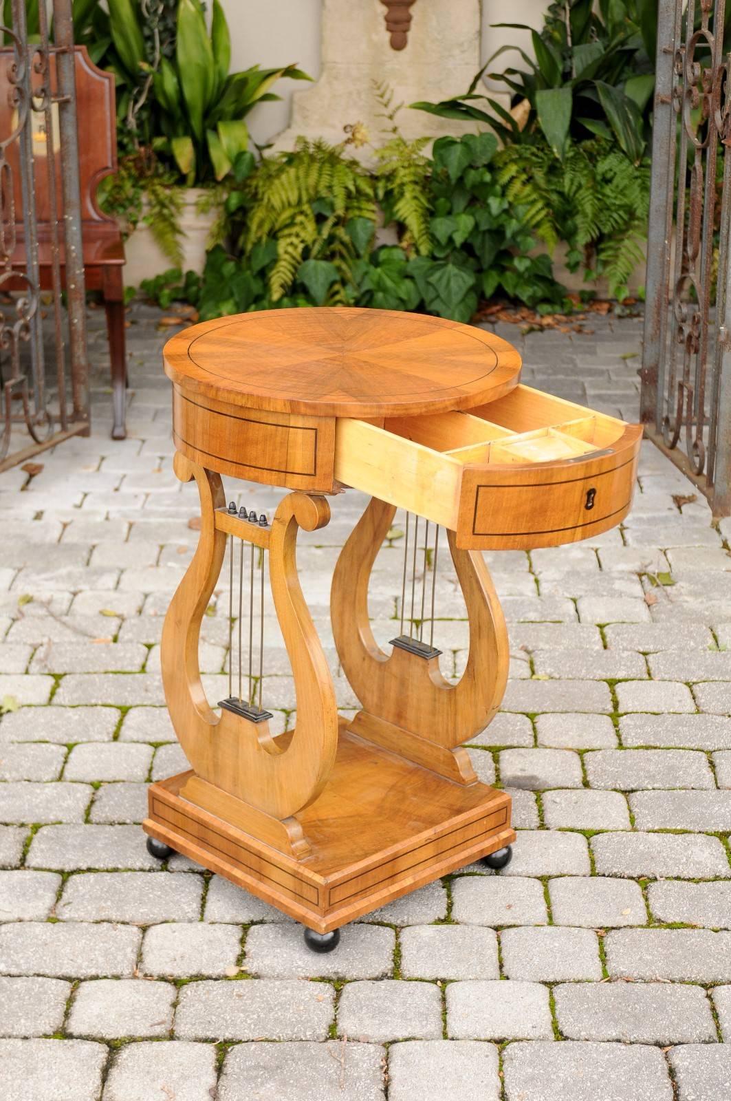 An Austrian Biedermeier period  table with lyre shaped legs and round top from the mid-19th century. This Biedermeier table circa 1840 features a circular top adorned with radiating veneer, surrounded by a dark banded inlay. The apron is decorated