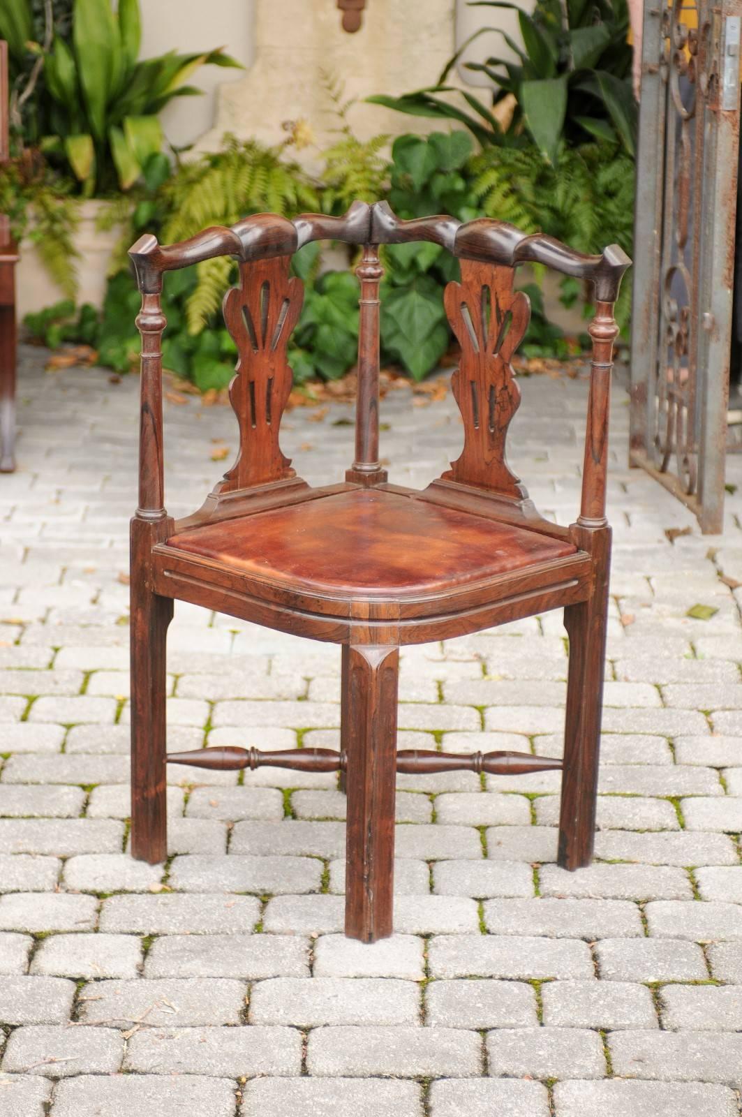 An English carved wood corner chair with leather seat from the mid-19th century. This English corner chair features a carved back with two pierced splats and supported by three thin columns. The warm brown leather seat is raised on four straight