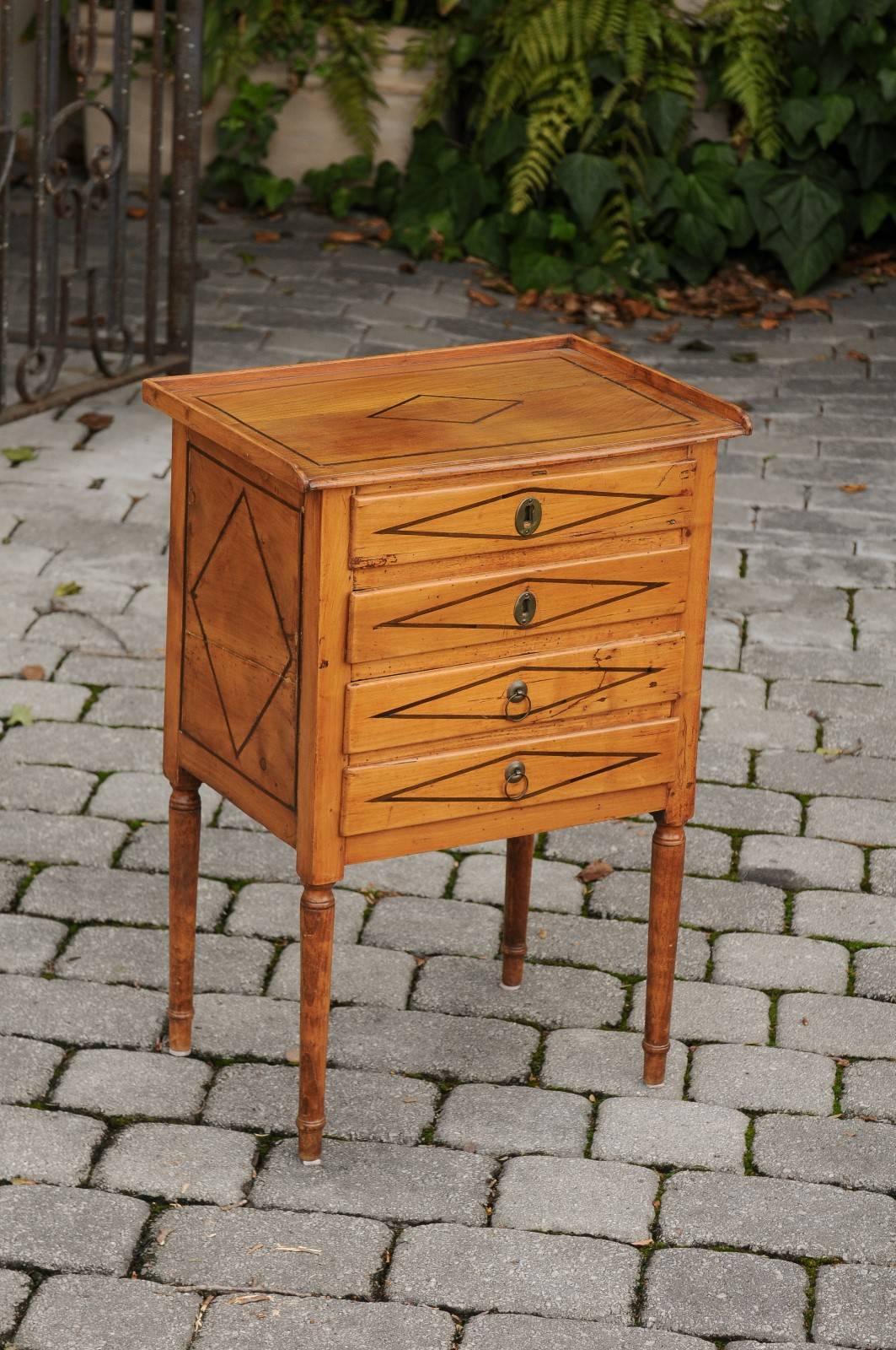 A petite French neoclassical fruitwood four-drawer commode from the early 19th century. This small size French commode from the 1820s features a three-quarter wooden gallery sitting atop four veneered drawers. These drawers are adorned with