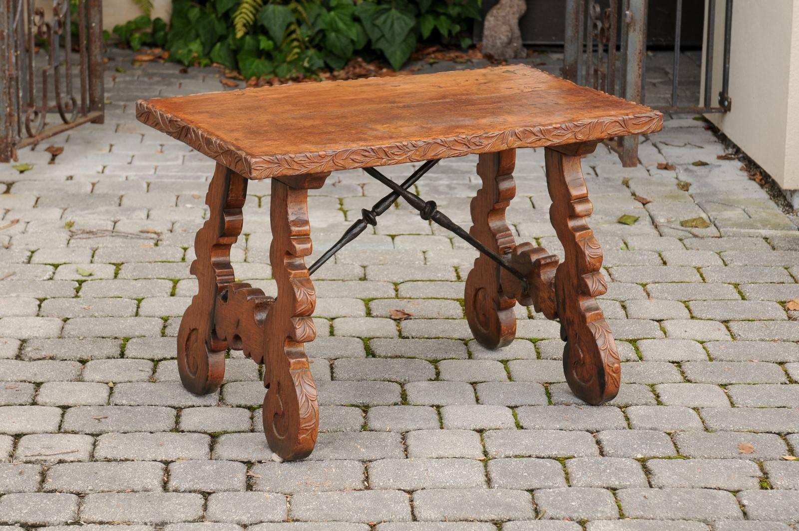 A French Baroque style oak trestle table with lyre shaped legs and iron stretcher from the early 20th century. This French low side table features a rectangular two-plank top adorned on its edge with a delicate foliage carving. The table is raised