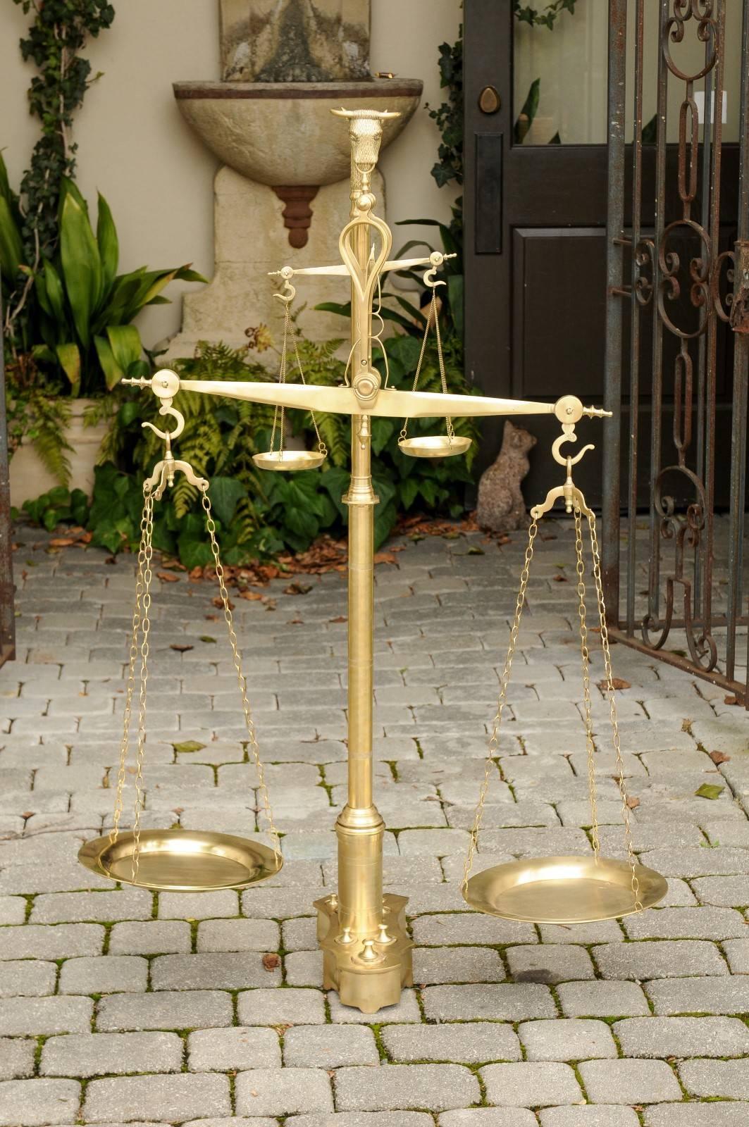 A Dutch two-tiered brass balance scale with its weights from the late 19th century. This large size brass scale was born in the Netherlands in the 1880s. Featuring a central beam supporting the various plates, the eye becomes immediately aware of