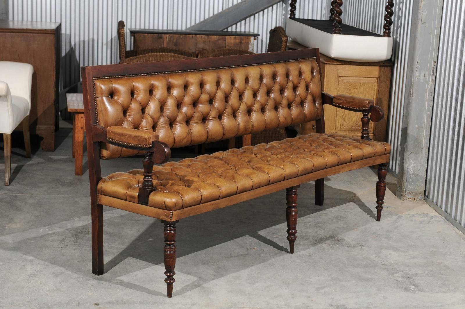 English tufted leather upholstered bench from the late 19th century, features a brown leather diamond-tufted upholstered back and seat with partially upholstered arms and brass nailhead trim. The slightly slanted back shows a perfect continuity with