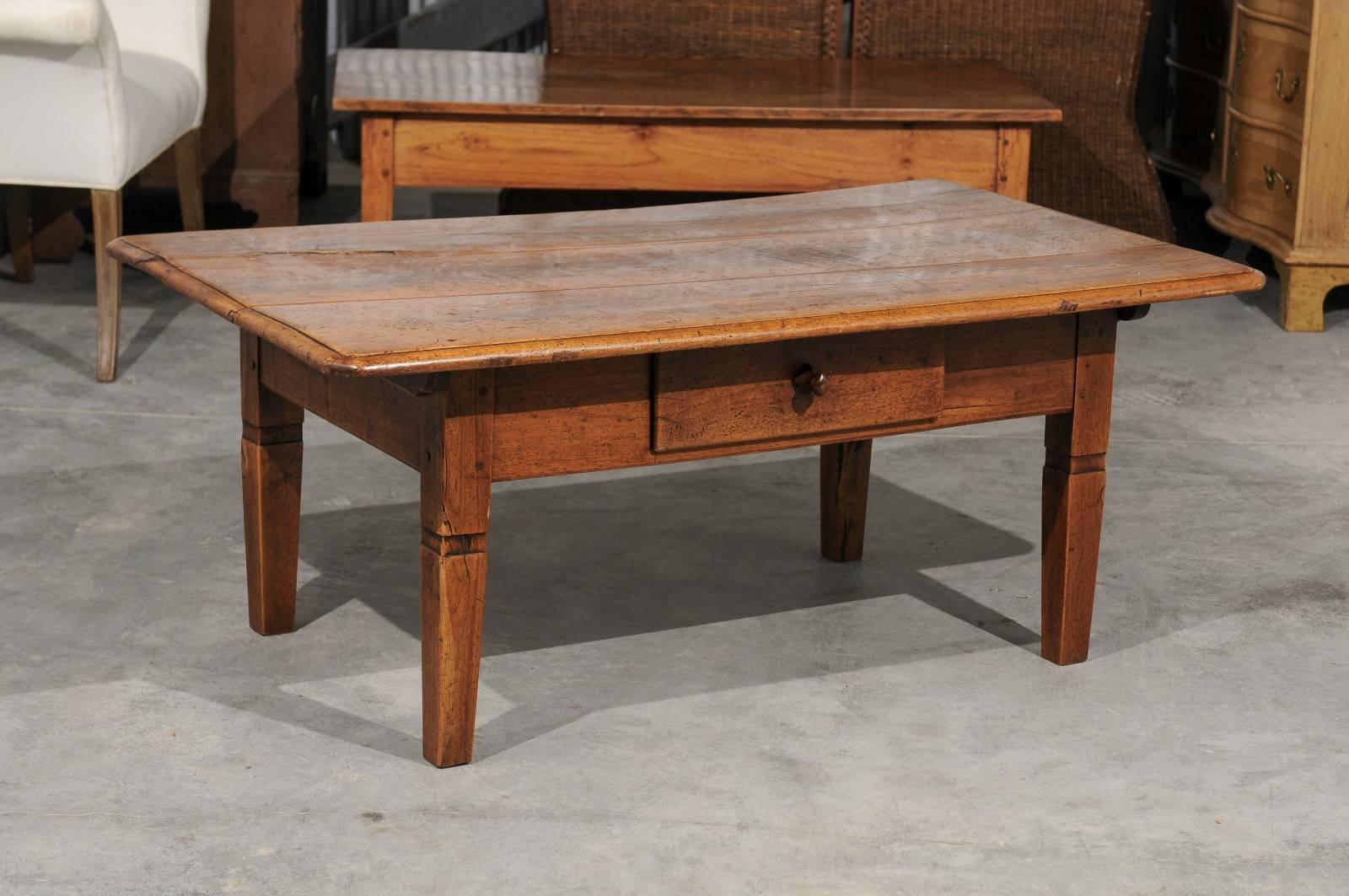 A French walnut (or cherry) coffee table with single drawer from the second half of the 19th century. This French wooden coffee table features a three-plank rectangular top with rounded edges and small chamfered corners. This simple top is raised on