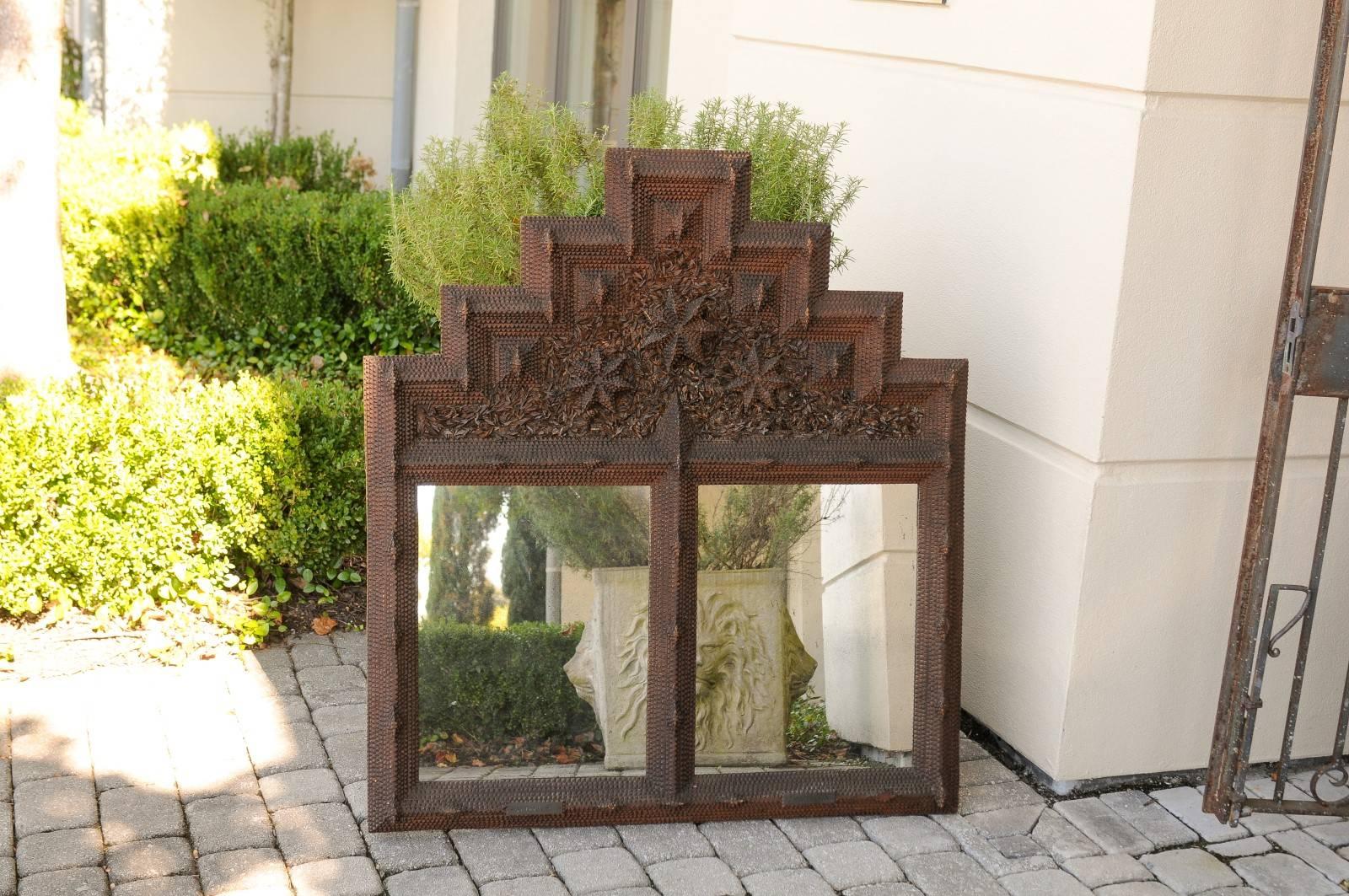 A French Tramp Art carved wooden mirror with double mirror panelling and stepped crest from the early 20th century. This French mirror was created in the early 1900s and features an exquisite stepped crest, carved in the traditional Tramp Art manner