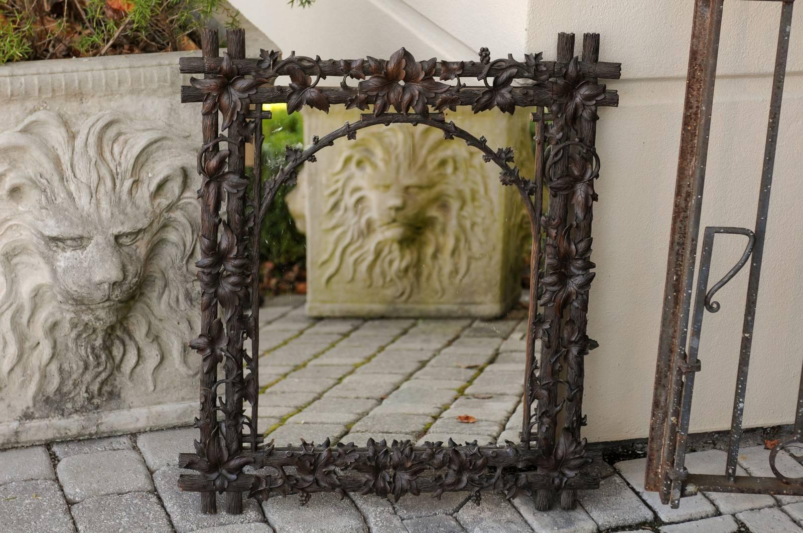 A German Black Forest wooden carved mirror with foliage motifs from the turn of the century. This German mirror was born in the early 1900s, and features an exquisite carved frame imitating branches around which are intertwined delicate vine leaves.