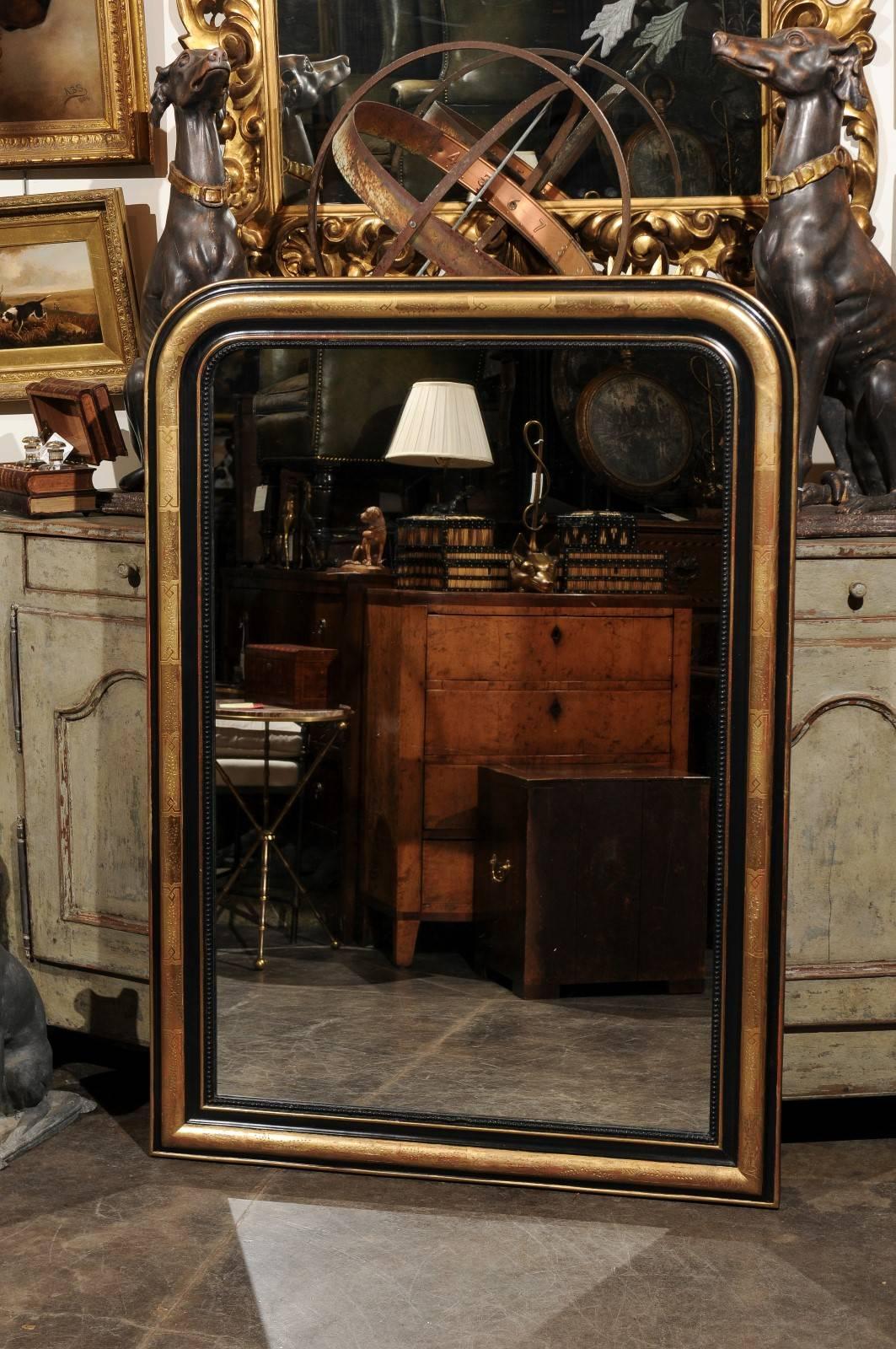 A French Louis-Philippe style black and gold wall mirror from the early 20th century. This French mirror features the typical Louis-Philippe Silhouette, with its simple, yet elegant vertical shape and rounded corners at the top. The mirror shows an
