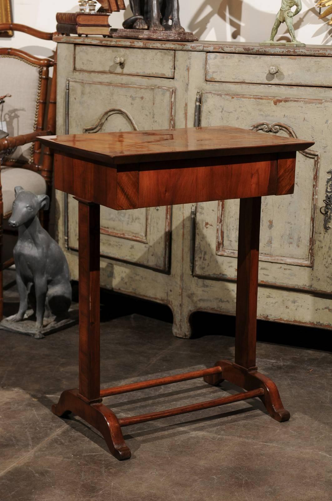 An Austrian Biedermeier walnut side table with frieze drawer and trestle base from the mid-19th century. This petite Biedermeier side table features a rectangular top sitting above a single dovetailed frieze drawer, hidden in the table's apron. The