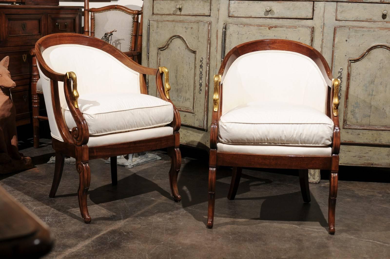 A pair of French Empire style upholstered tub chairs with swan motifs from the second half of the 19th century. Each of this pair of French fauteuils features a wraparound back terminated with exquisite pierced arms. These arms are made of S-scroll