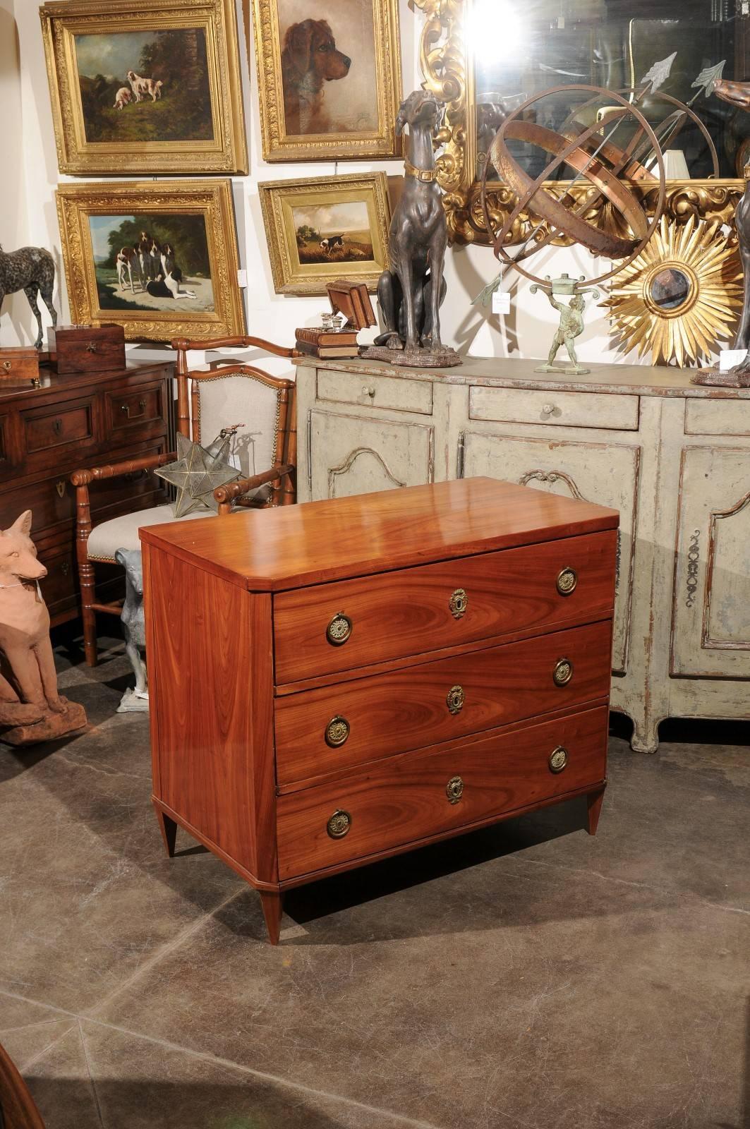 An Austrian Biedermeier period three-drawer commode from the mid-19th century. This Biedermeier chest features a rectangular top with canted corners in the front, above three dovetailed drawers. Each drawer is adorned with brass ring pulls and
